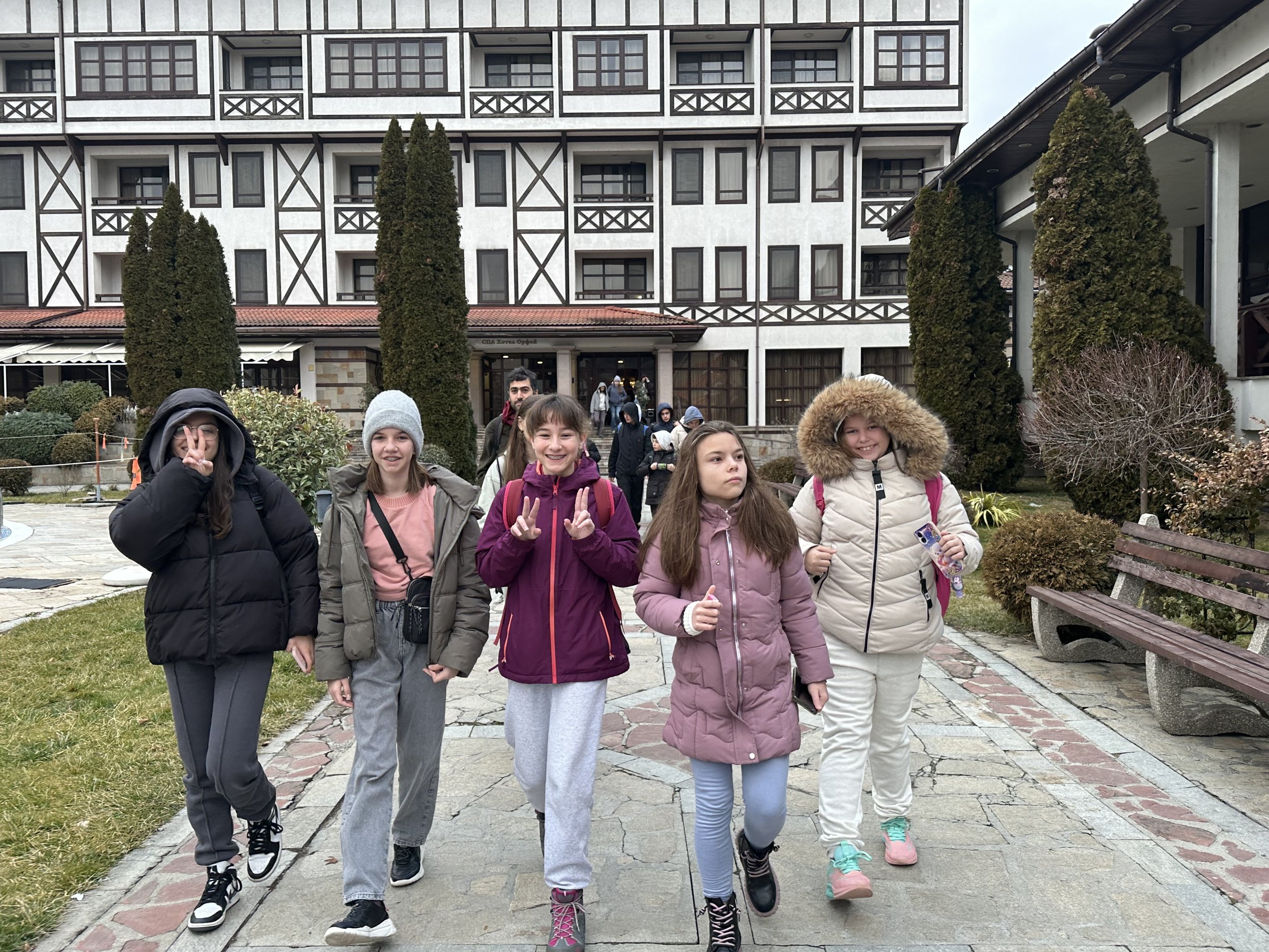 Group of children in winter clothing walking on a path in front of a building with a traditional architectural style.