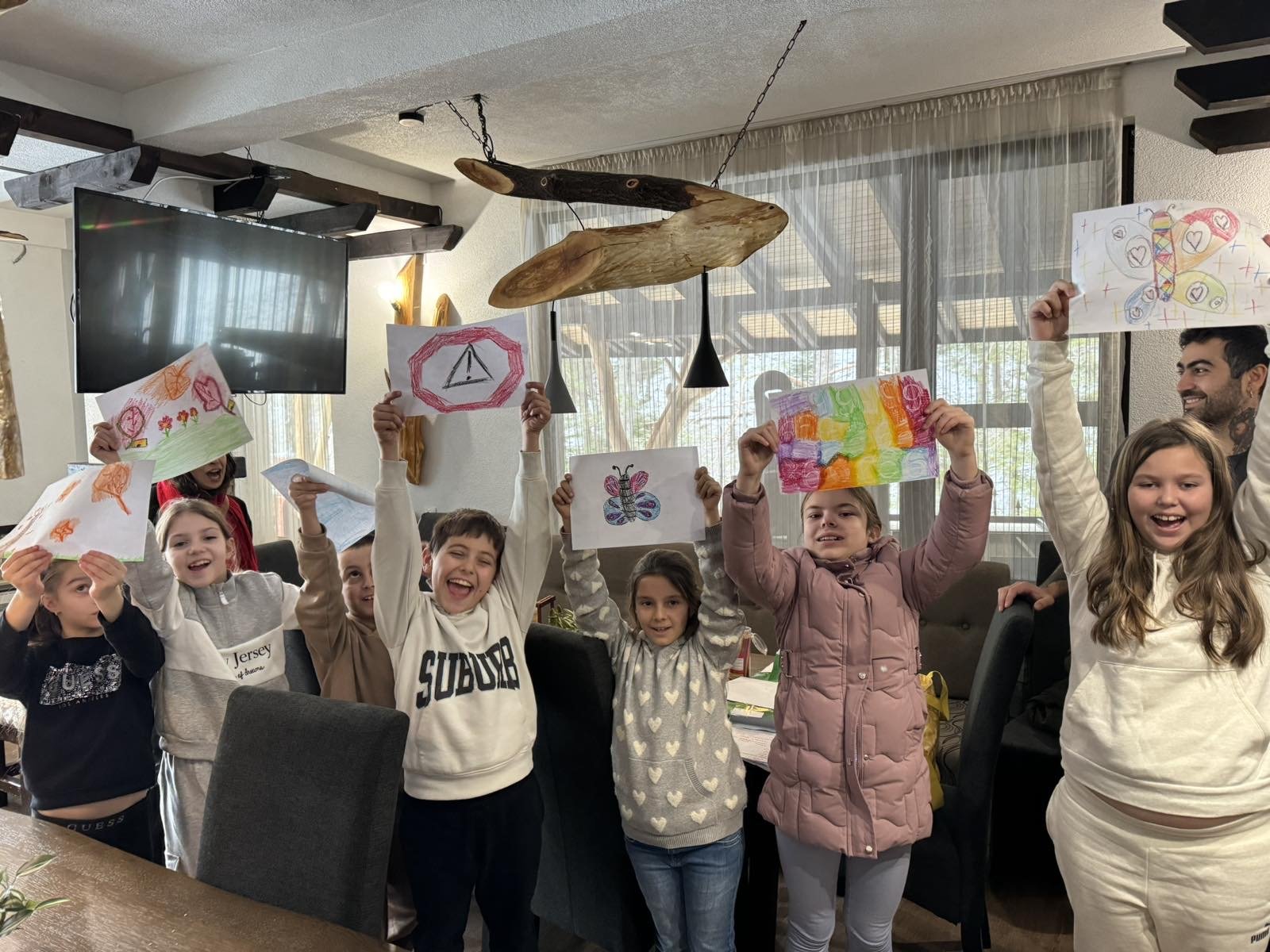 Group of smiling children holding colorful drawings indoors