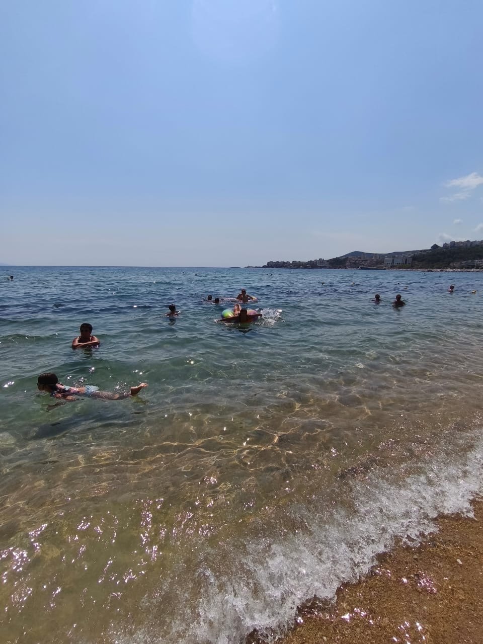 Children at Camp Evolve International swimming and playing in the sea in Kavala, Greece, enjoying the sunny weather near a sandy beach during a fun group activity.
