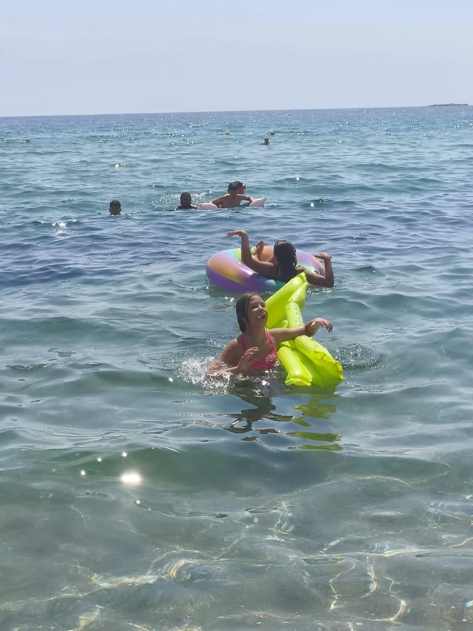 People swimming and floating in the ocean on a sunny day, with clear water and distant horizon.