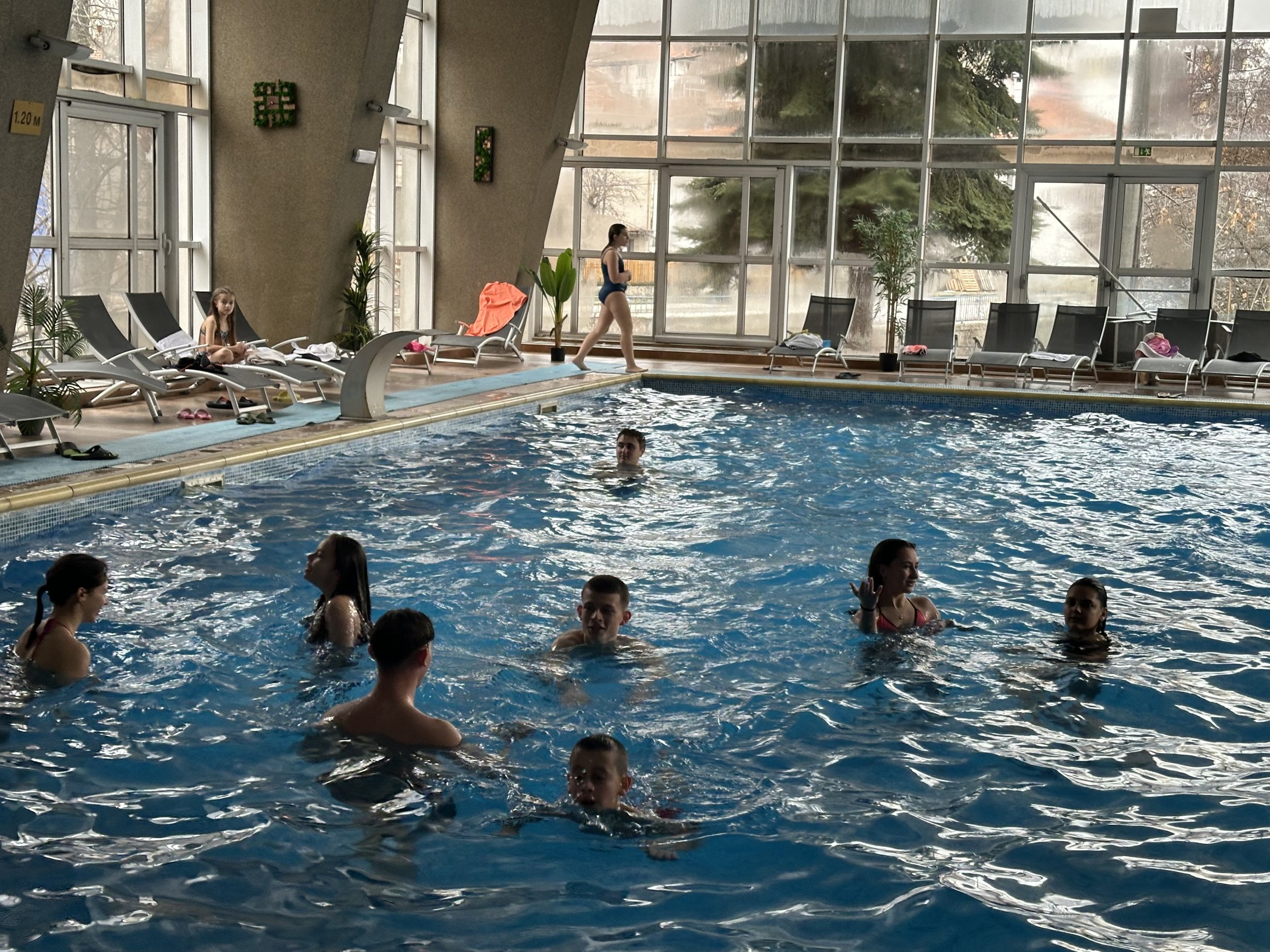Indoor swimming pool with people swimming and relaxing on lounge chairs