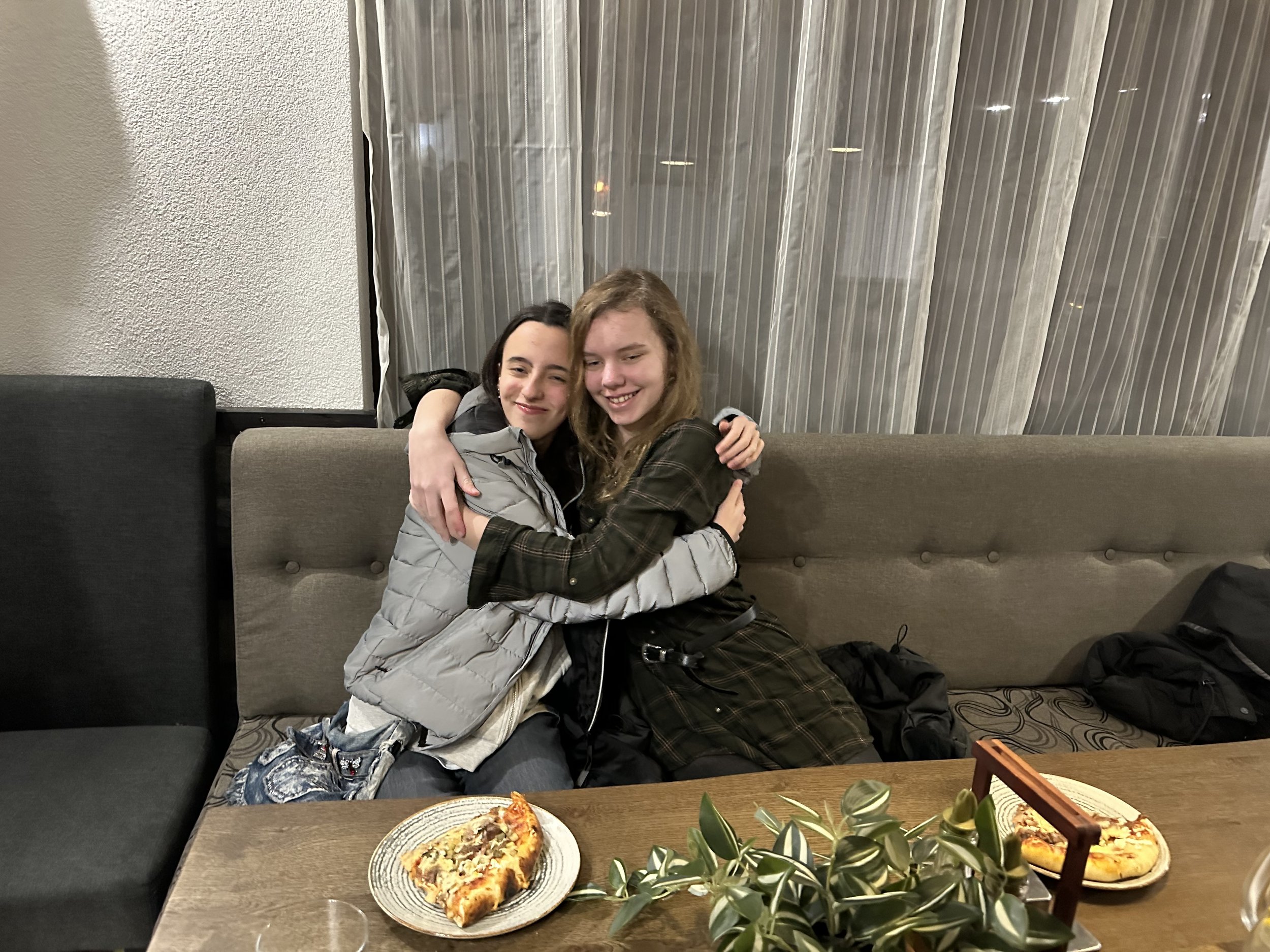Two people hugging and sitting on a gray sofa at a dining table with plates of food and greenery decoration.