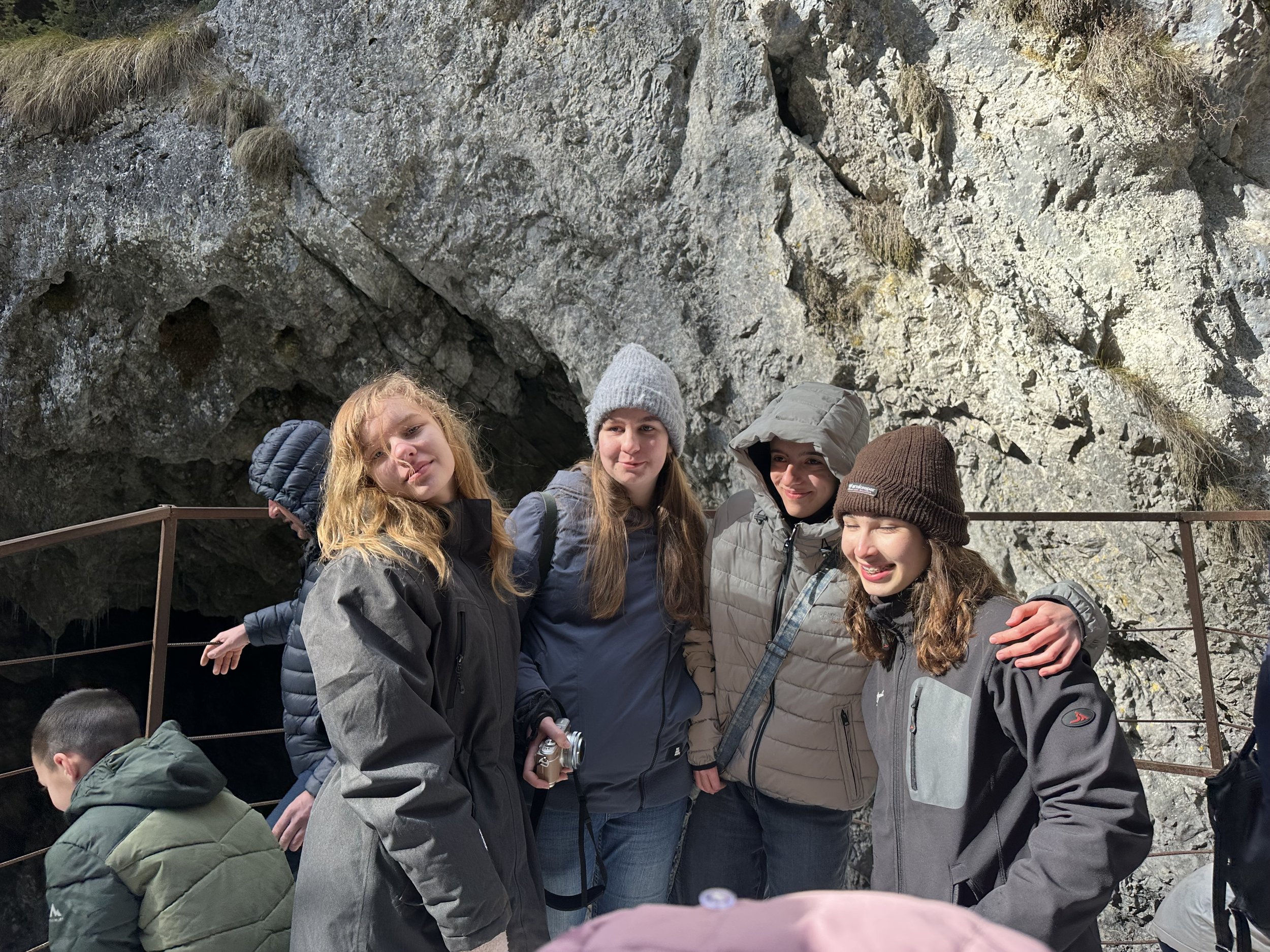 Group of people in winter clothing standing in front of a rocky cave entrance.