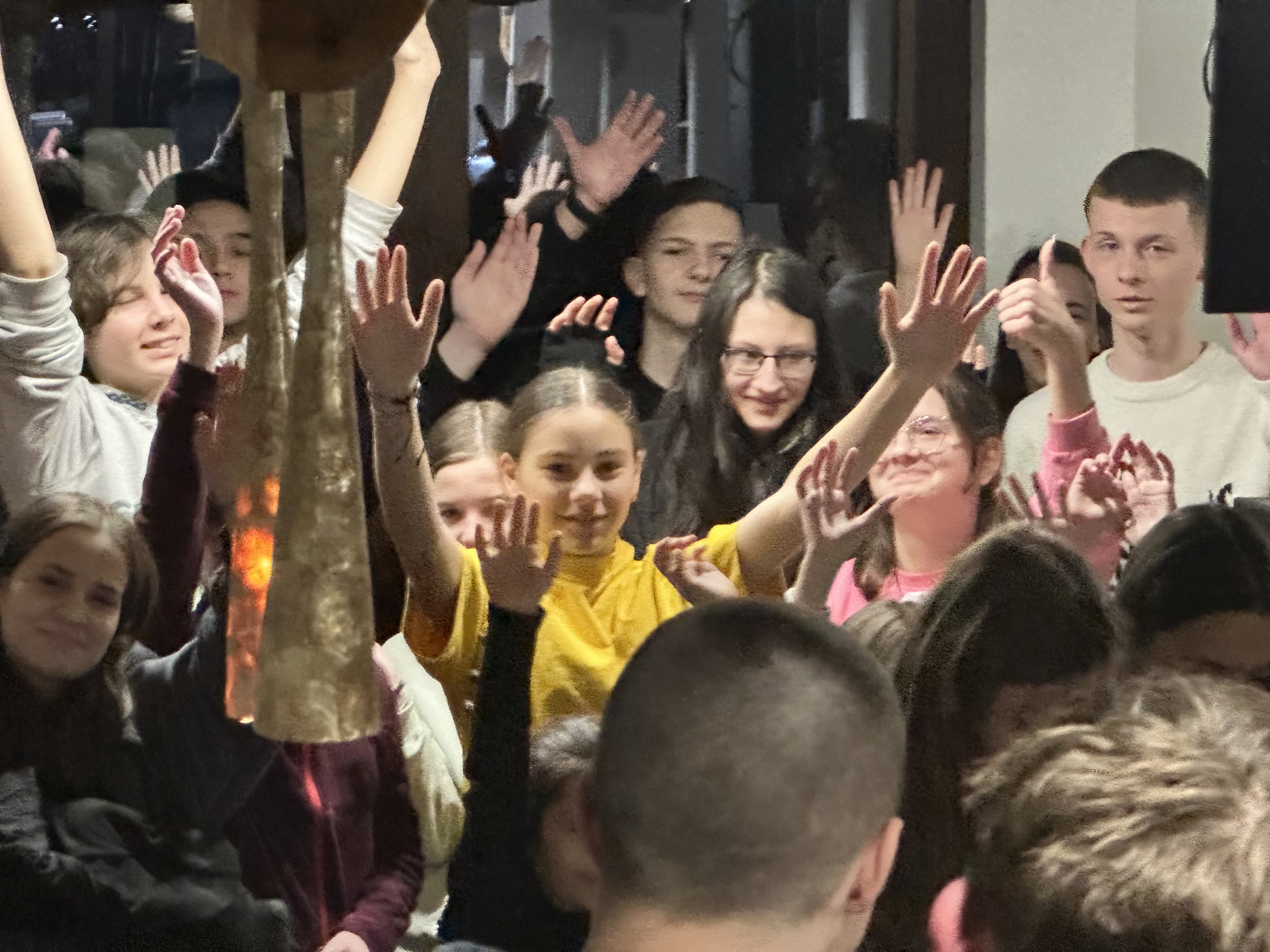 A group of people indoors with hands raised, appearing to participate in an activity or event.