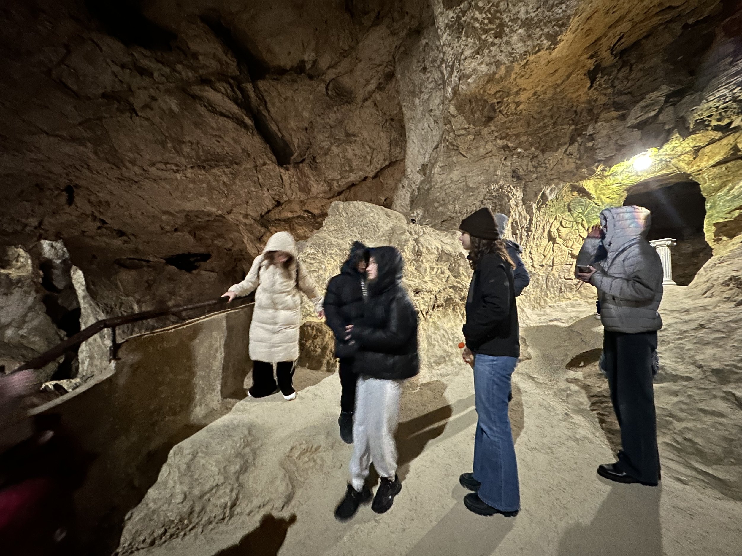 Group of people exploring a cave with rocky walls and dim lighting.