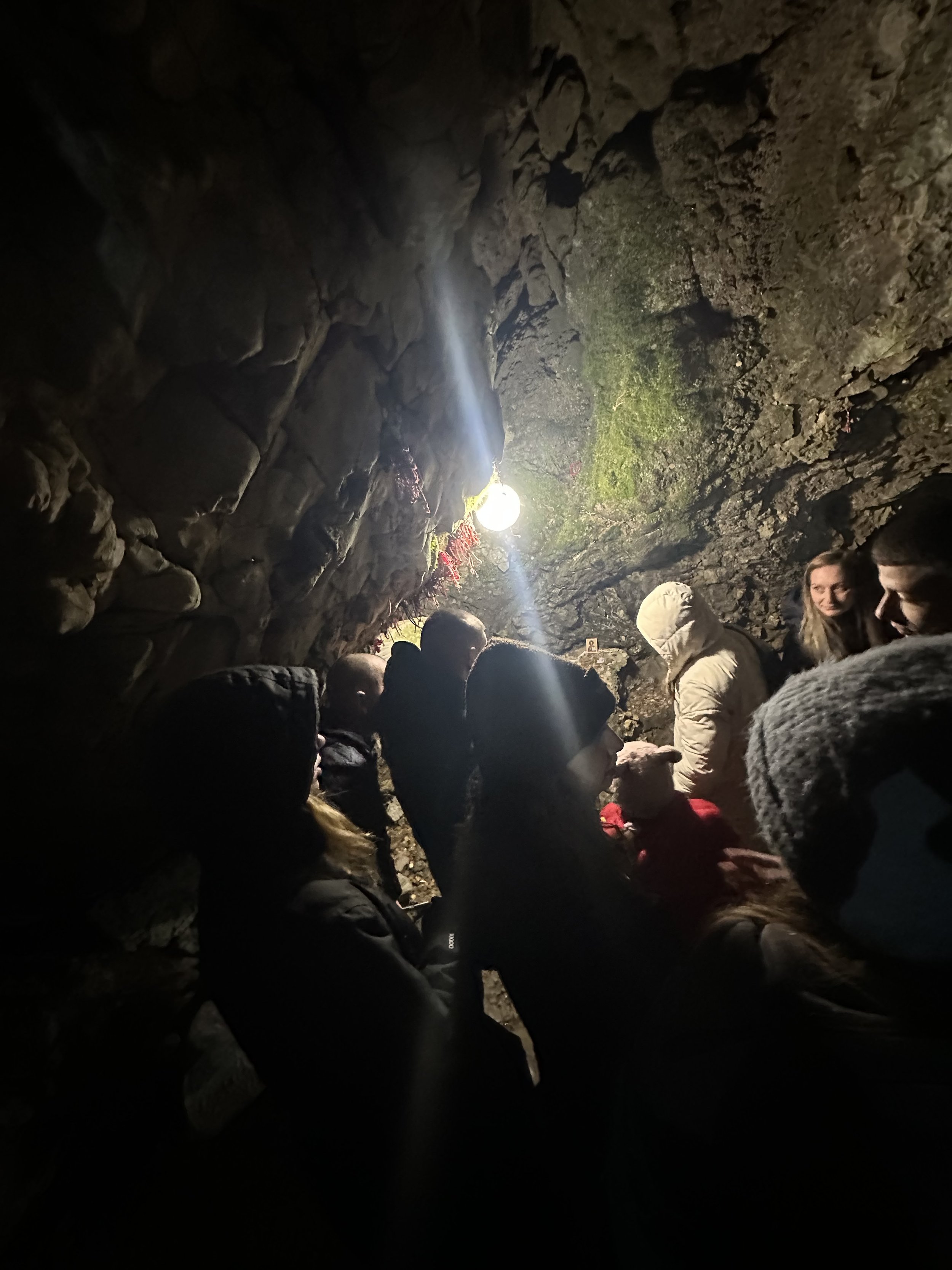 Group of people in a dimly lit cave with a lightbulb overhead, rocky walls, and visible moss.