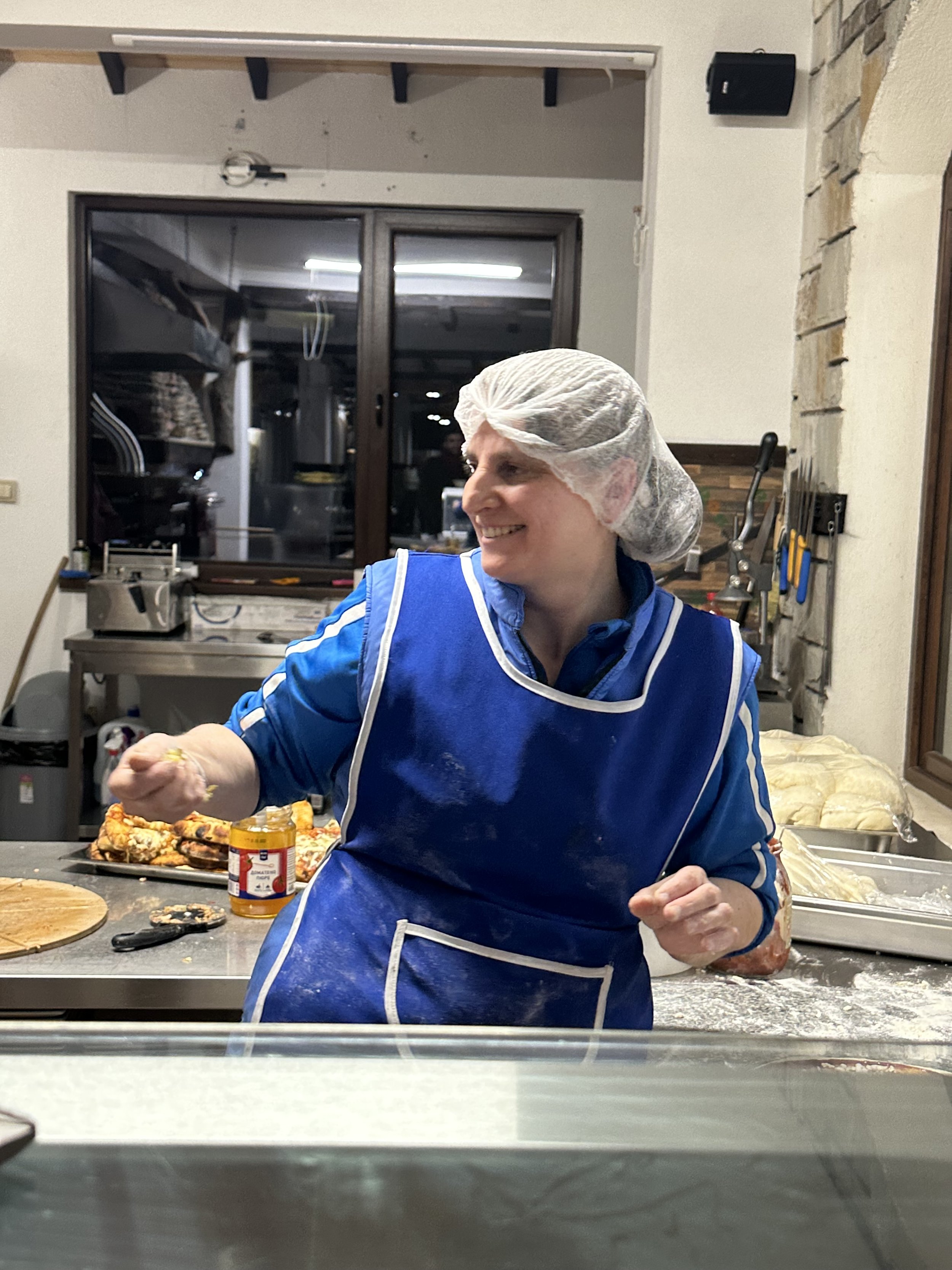 A person wearing a hair net and blue apron preparing food in a kitchen.