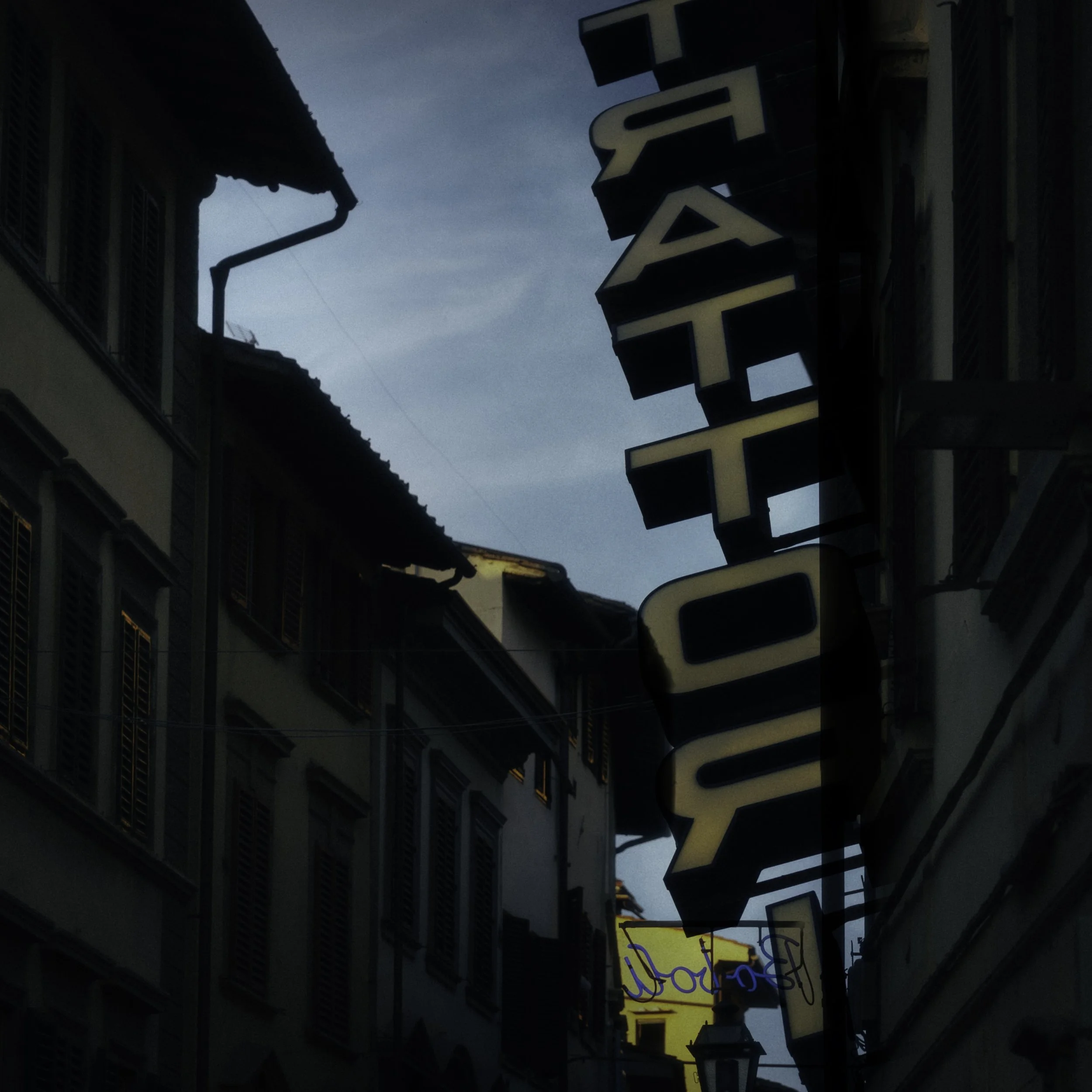 A narrow street lined with old European-style buildings, with a vertical sign that reads 'RESTAURANT' in capital letters.