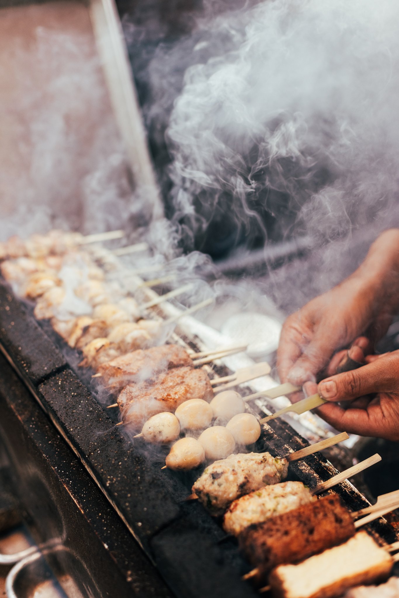 Skewers of meat and vegetables cooking on a grill with smoke rising.
