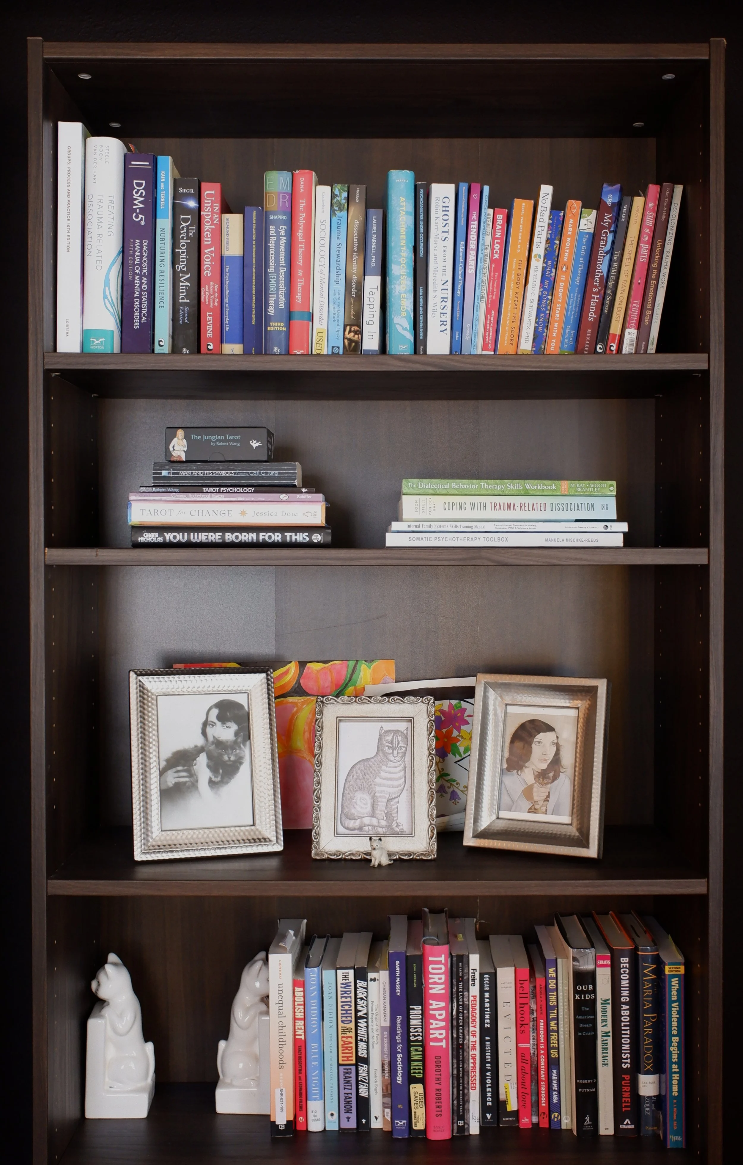 A dark wood bookshelf filled with books, framed photographs, and decorative items on four shelves.