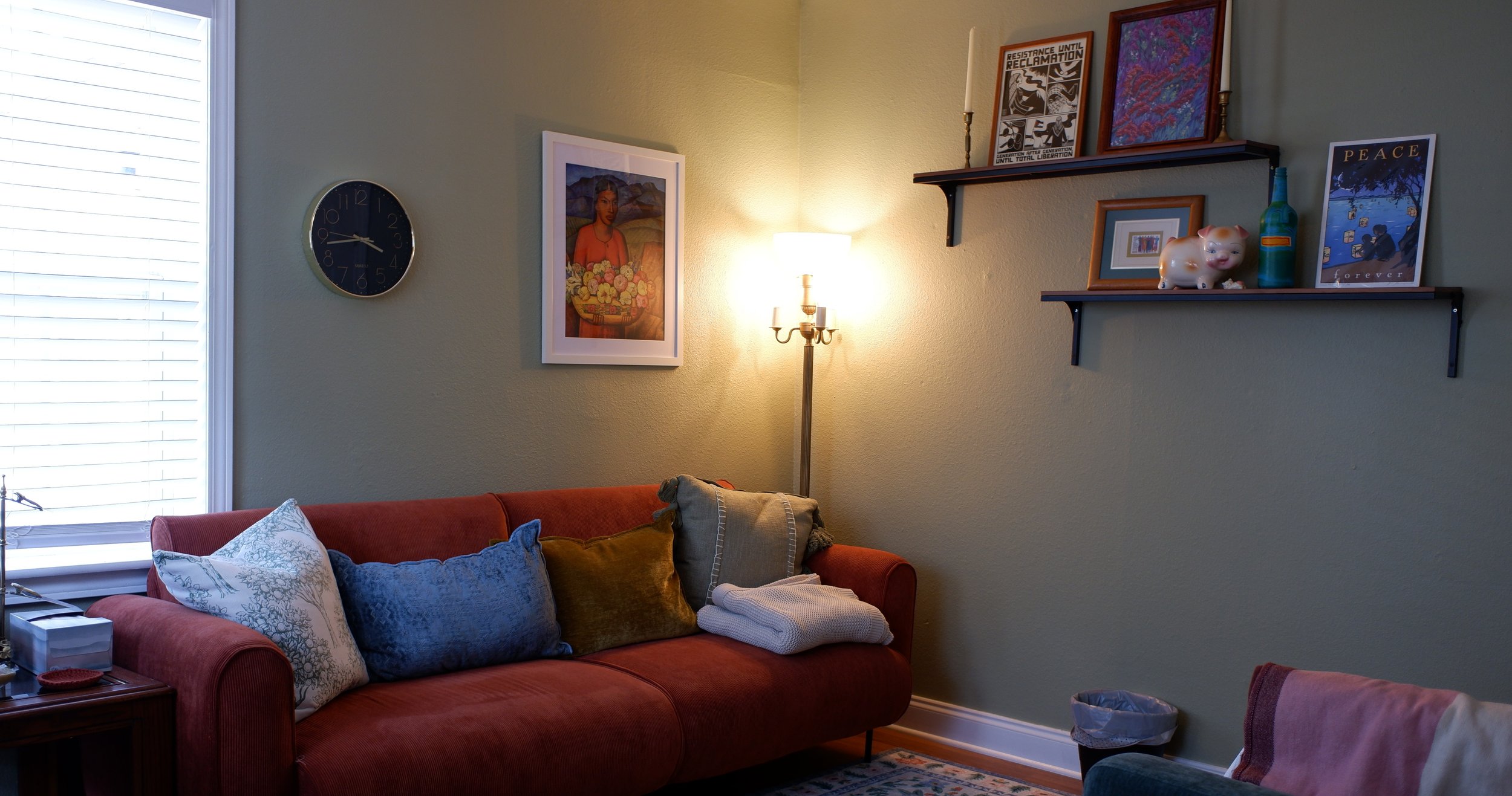 Living room with a red sofa, decorative pillows, a lamp, wall art, and shelves with framed pictures, figurines, and decorative items.