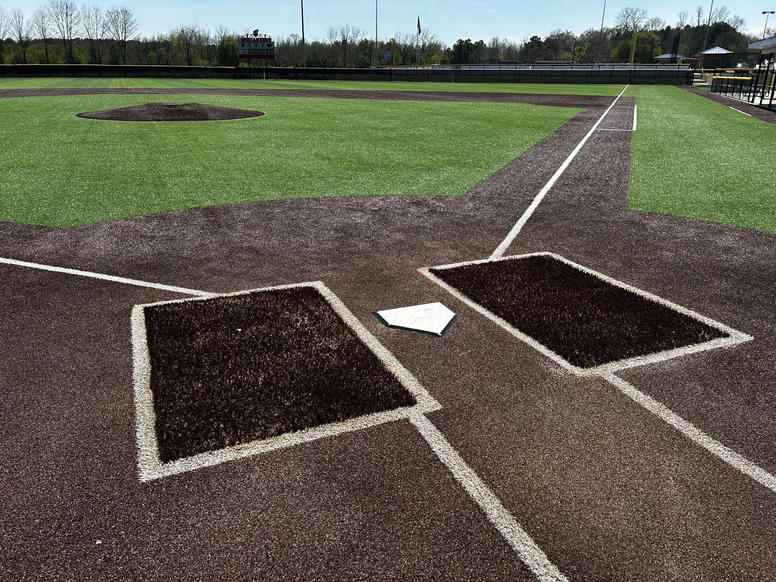 Baseball field focusing on home plate and batter's boxes, with a view of the pitcher's mound and outfield.