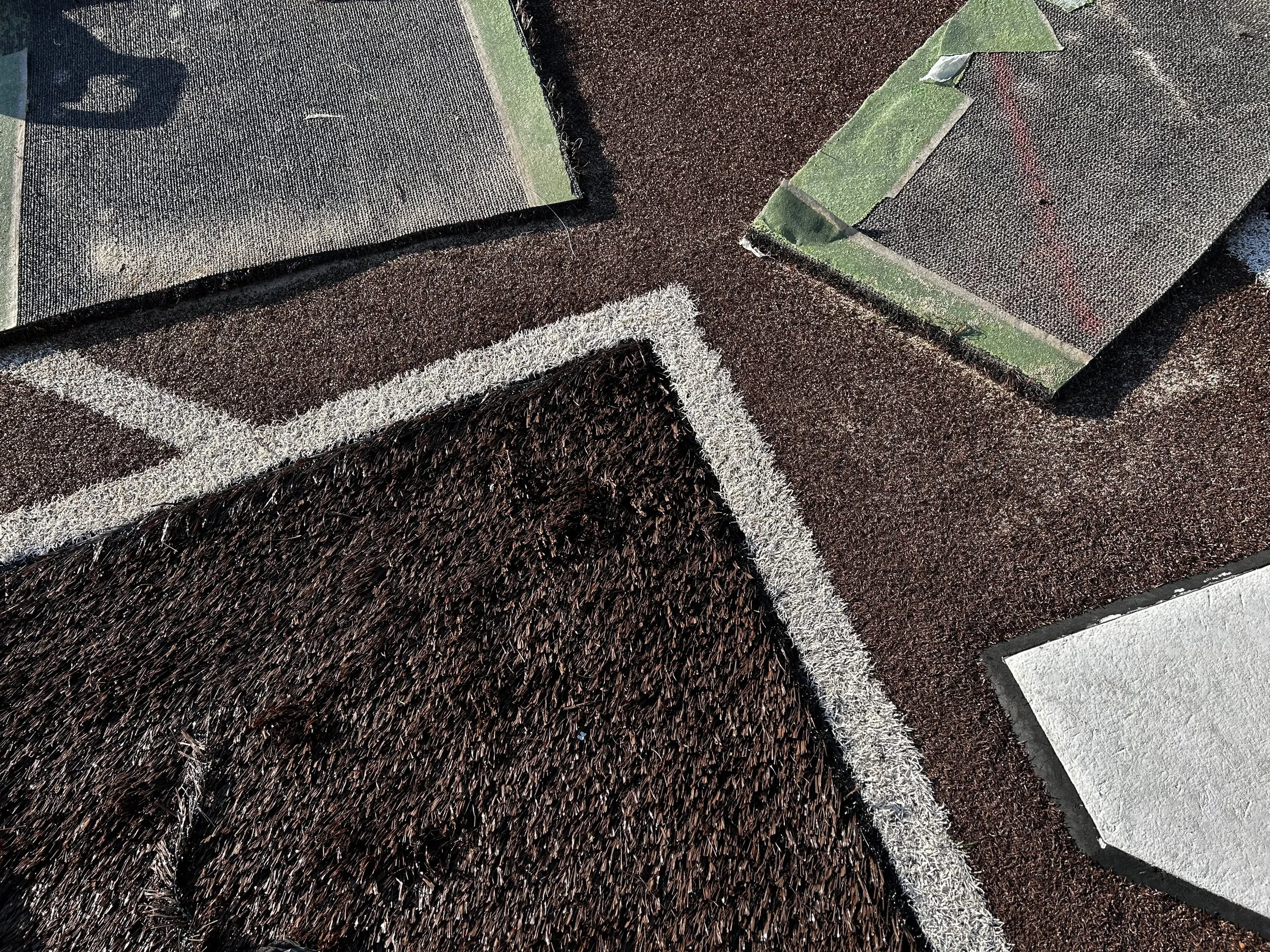 Artificial turf field with brown infill, white line markings, and removed sections showing the turf backing.