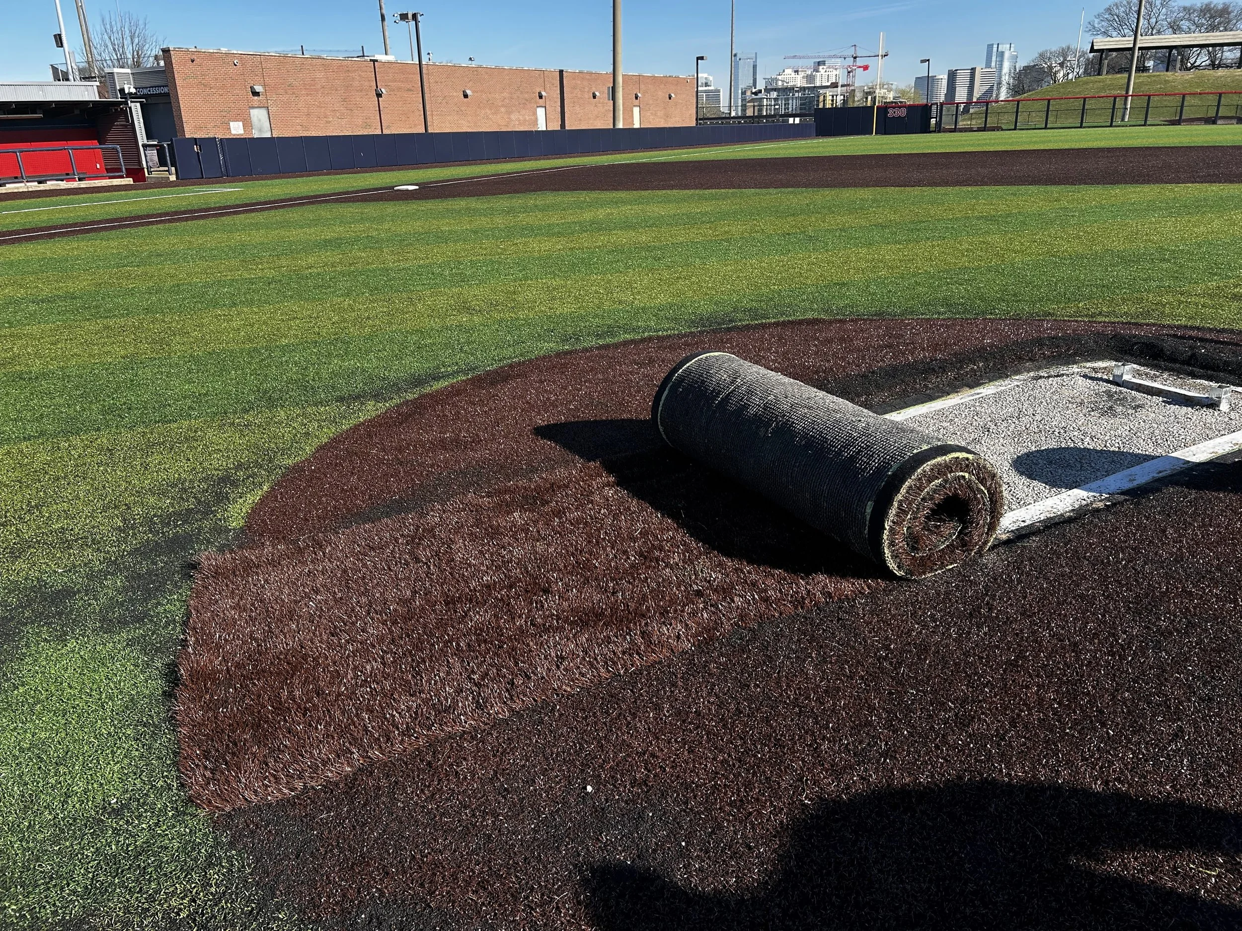 Baseball field with artificial turf and a roll of turf near a pitcher's mound area.
