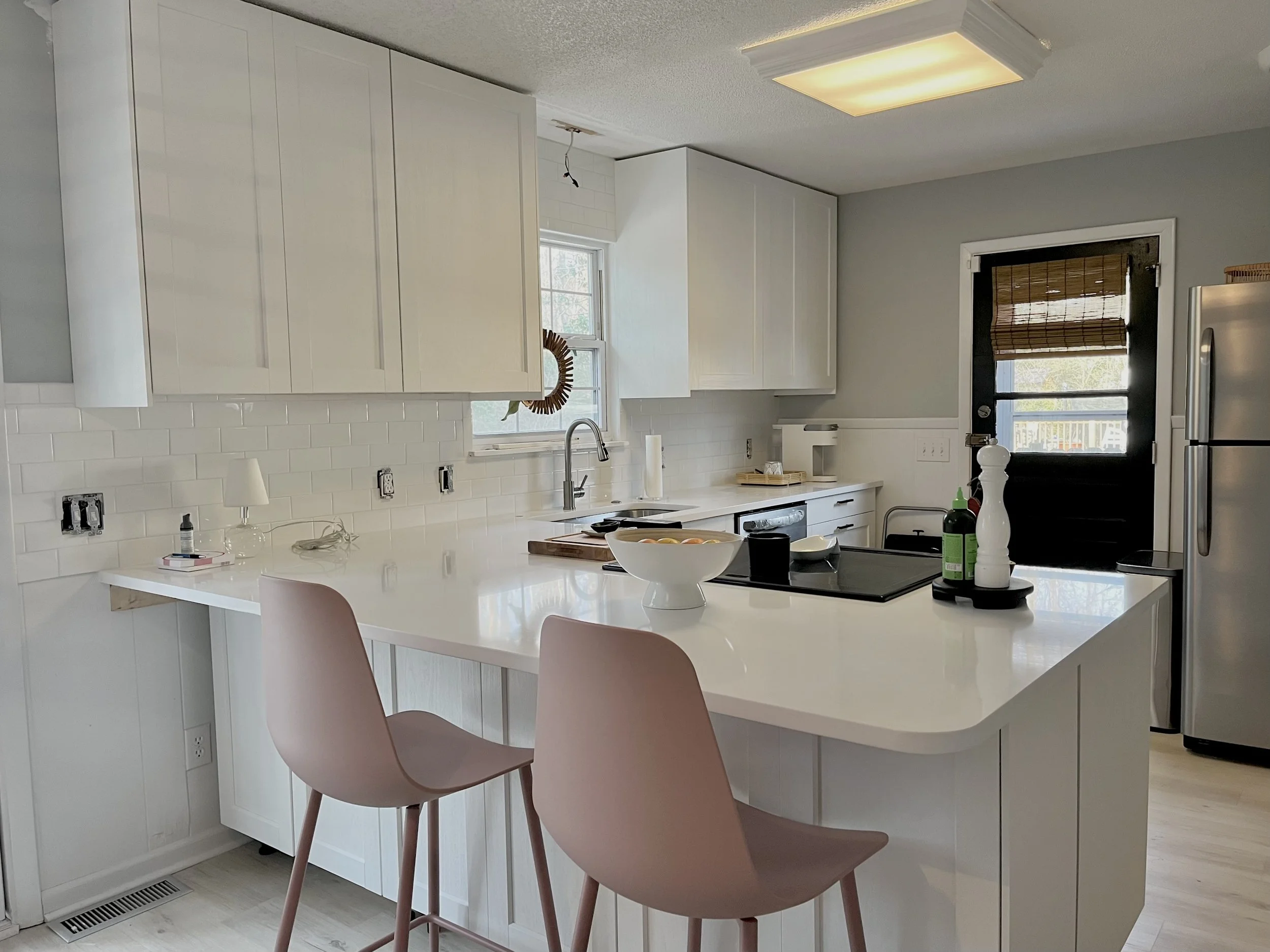 Bright white kitchen with a broad island, soft pink chairs, stainless appliances and light countertops