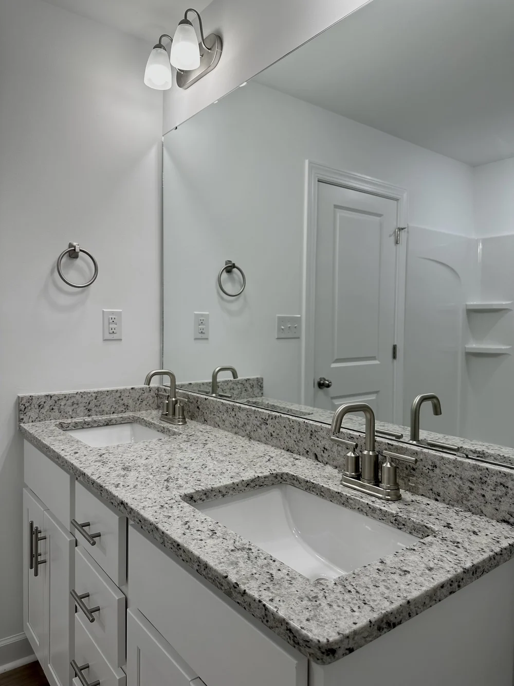 Double bathroom vanity with a speckled stone countertop, two rectangular undermount sinks and matching rear and side splashes