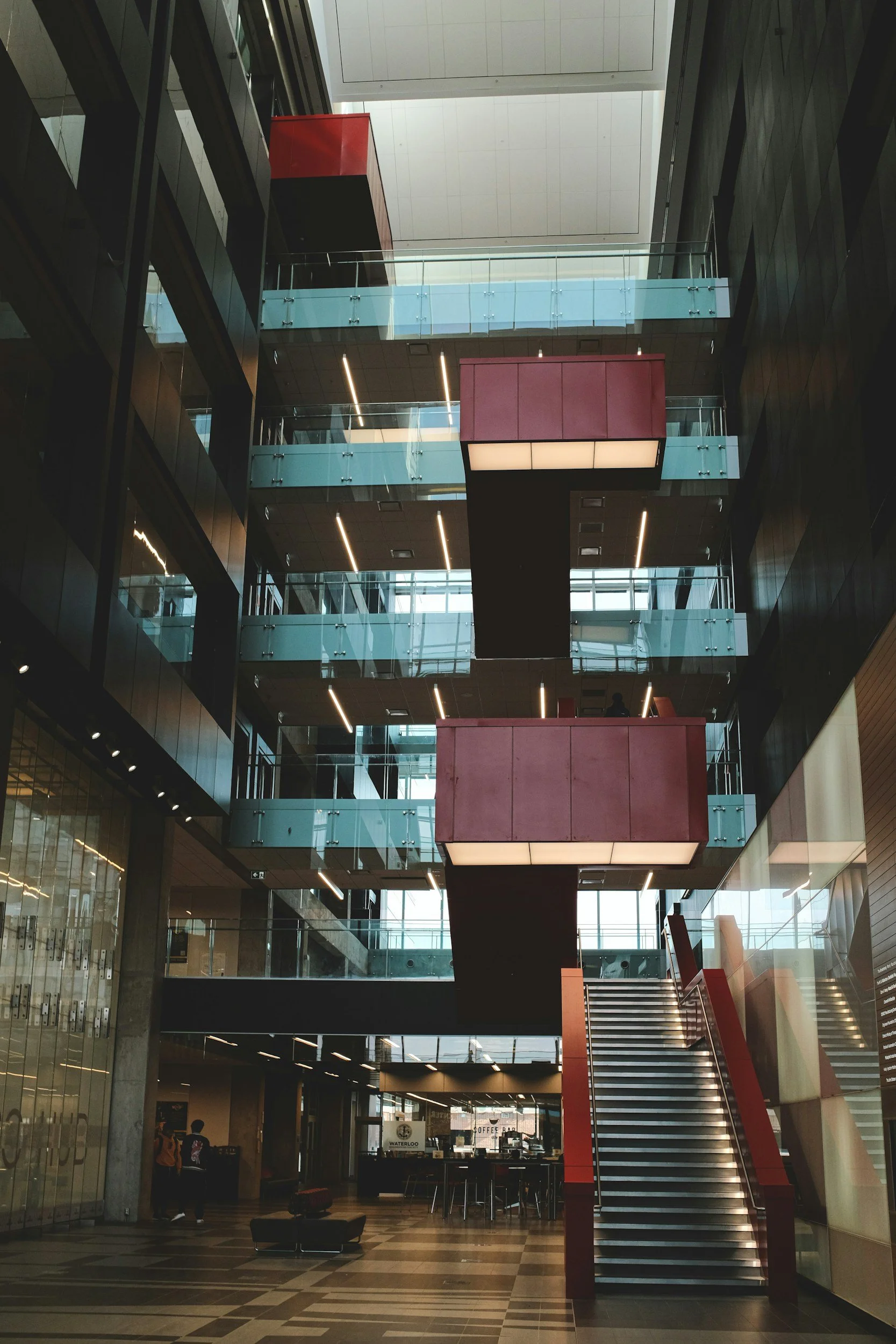 Interior view of a modern multi-level building lobby with stairs, glass balconies, and a coffee shop at the ground level.