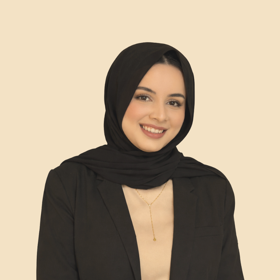 A young woman with light skin, smiling, wearing a black hijab, a black blazer, and a beige top, against a neutral background.