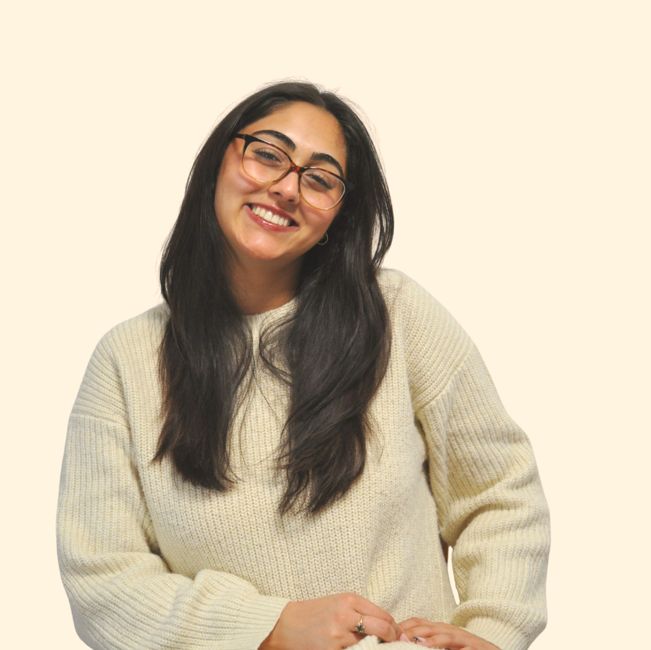 Smiling woman with glasses wearing a cream sweater, posing against a plain light background.
