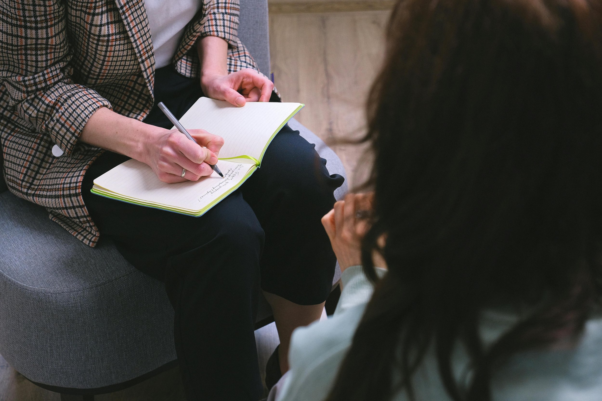 A person taking notes in a notebook while talking to another person in a therapy or counseling session.