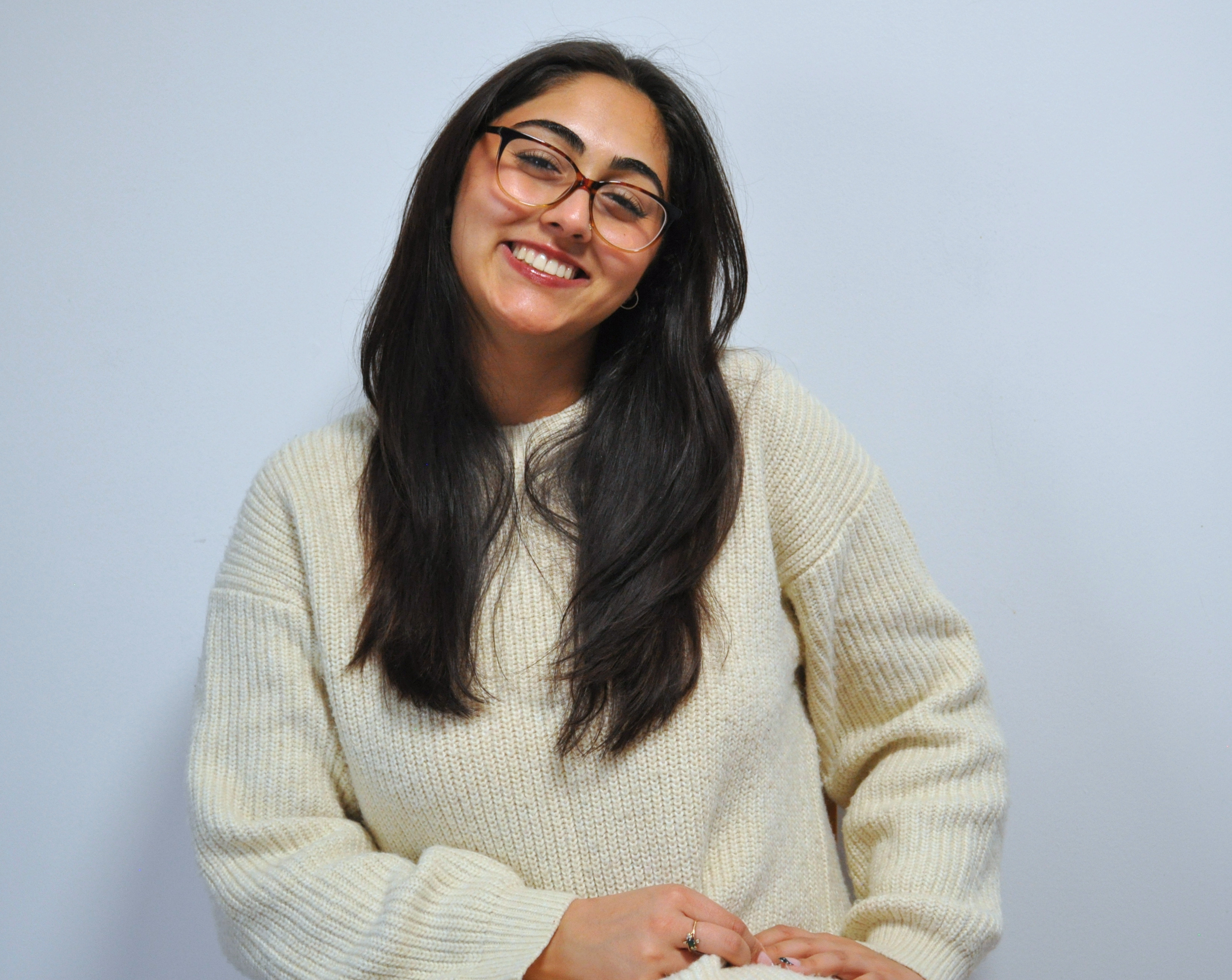 Smiling woman with glasses wearing a cream sweater, posing against a plain light background.