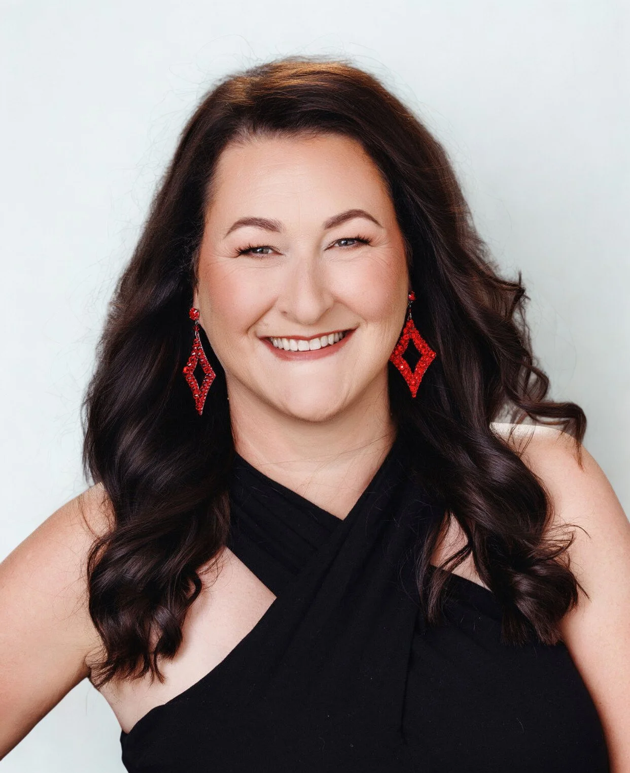 A woman with shoulder-length brown hair wearing a black sleeveless top, smiling at the camera against a white background.