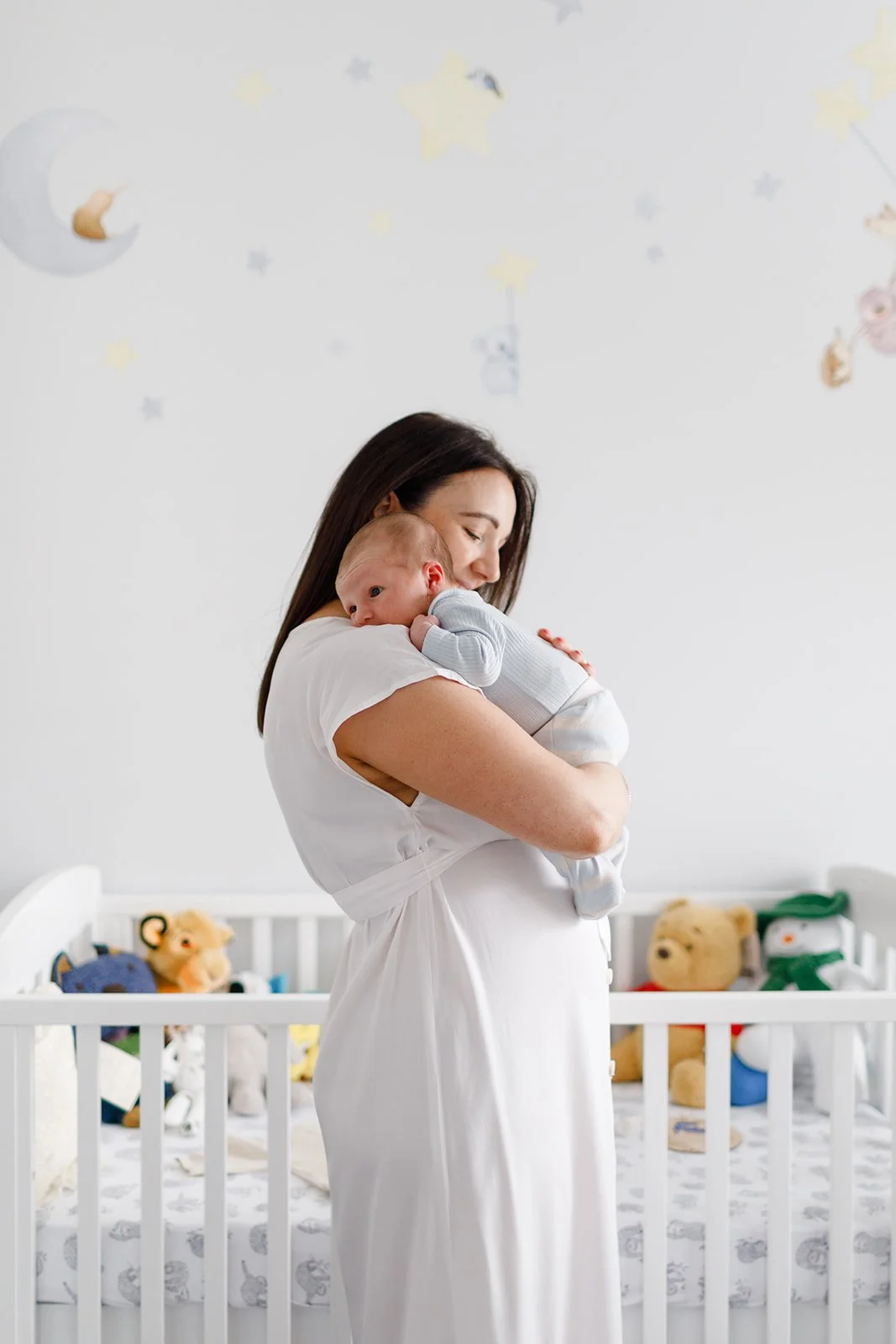 Meg holding her newborn baby close, standing in the nursery filled with soft toys.