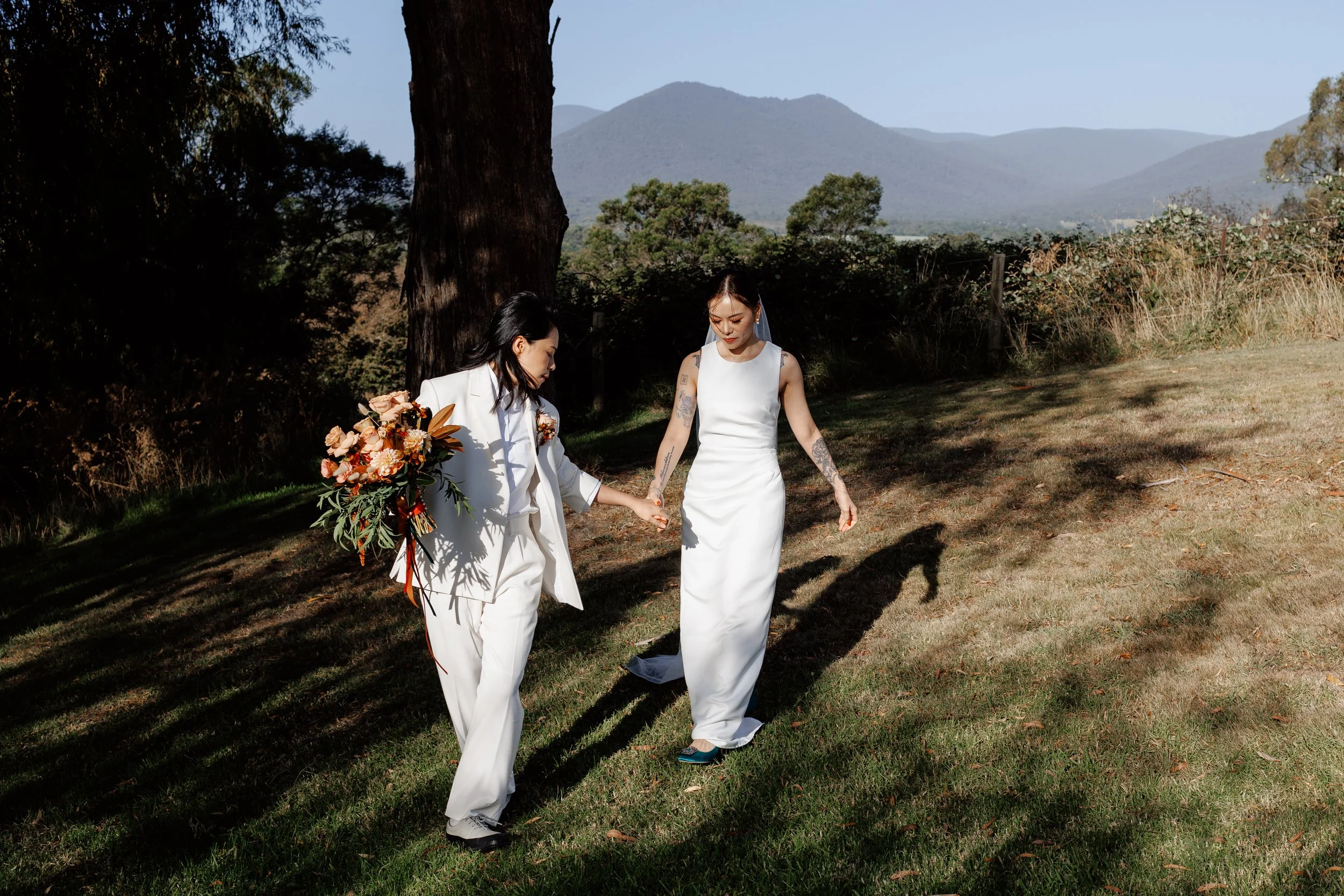 Vikki and Miffra walking hand in hand at their Riverstone Estate wedding in Healesville, smiling with joy.