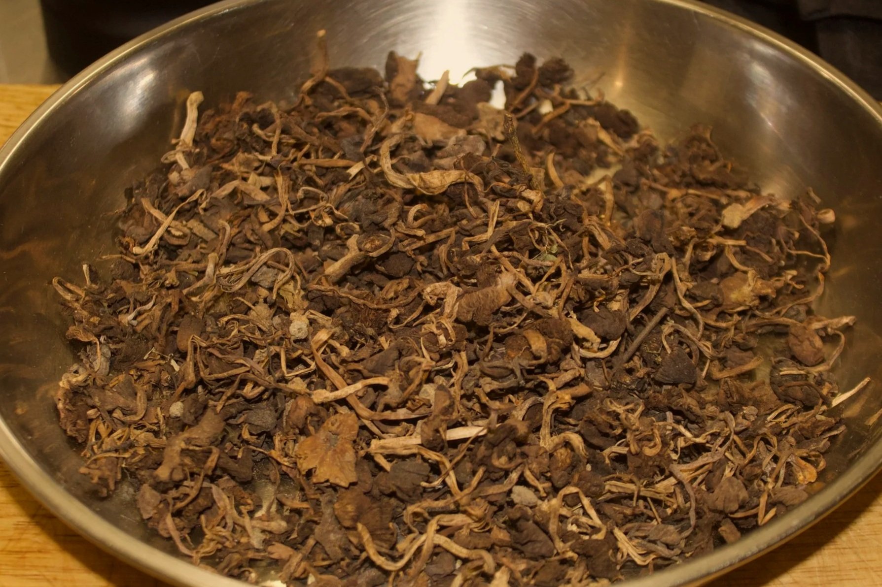 Dried Haitian djondjon black mushroom in a metal bowl on a wooden surface.