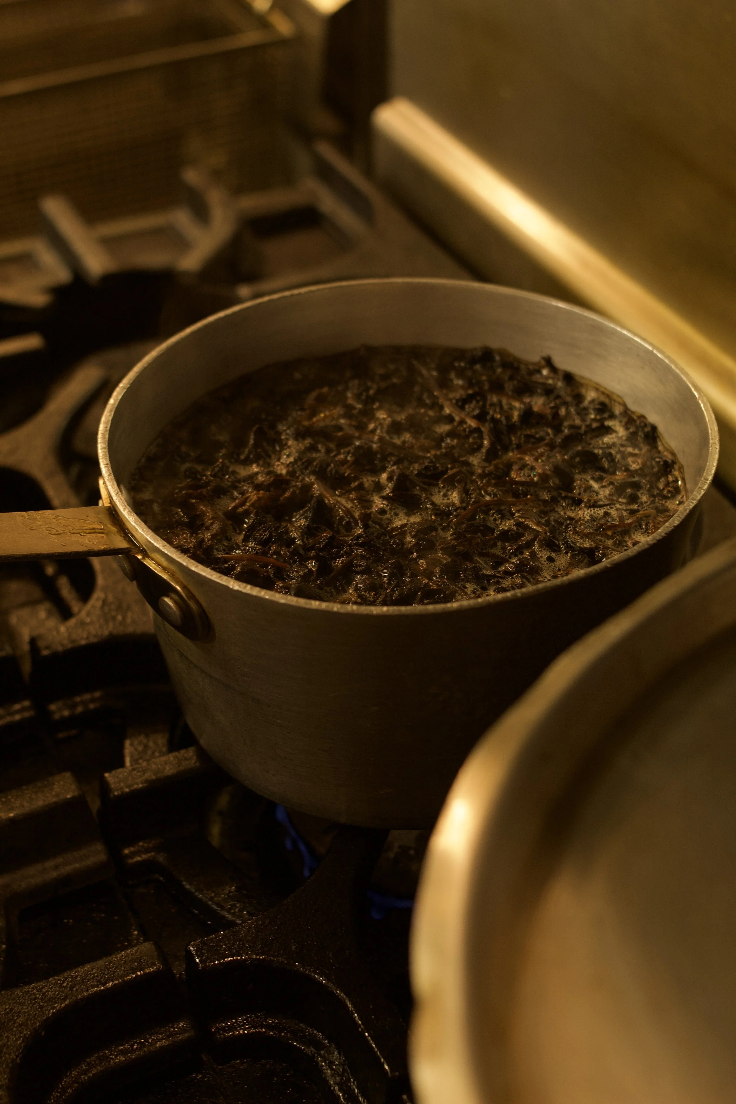 A pot on a stovetop simmering with a dark liquid and shredded Haitian djondjon black mushroom.