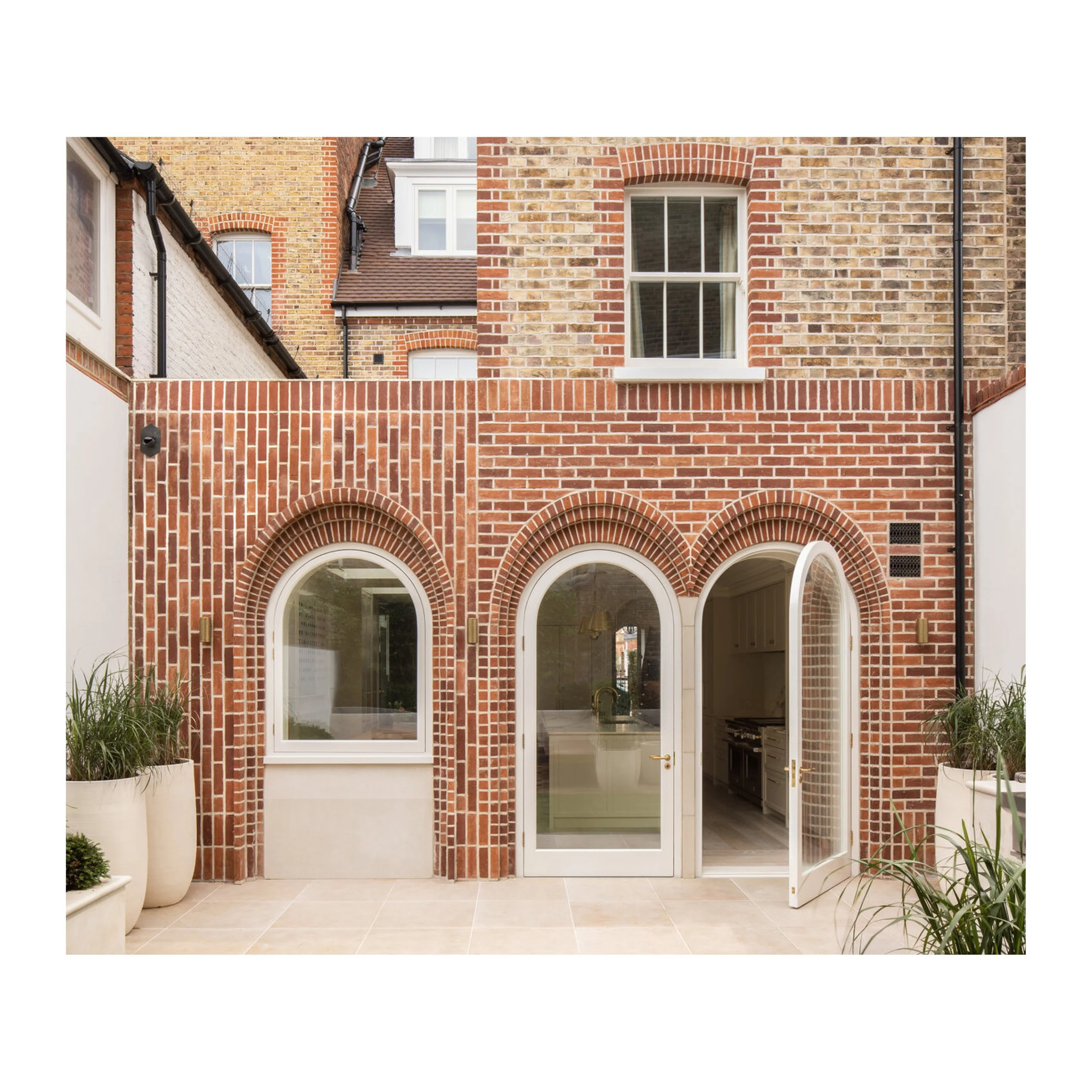 Craig Smith Architects — Back of a London terrace with a modern brick extension. Red brick walls, arched windows and doors with white painted timber frames and a small section