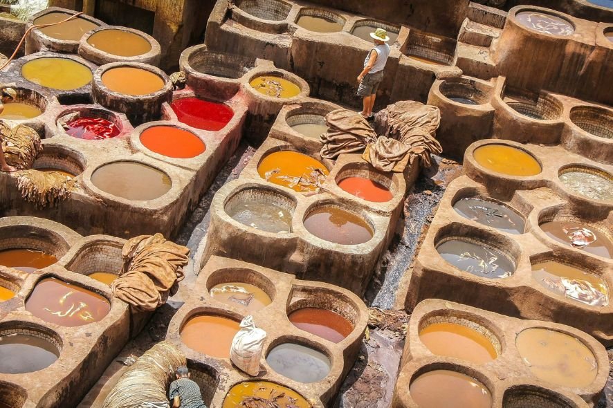 Traditional leather dyeing pits with various colored dyes, and workers using fabrics or hides in the process.
