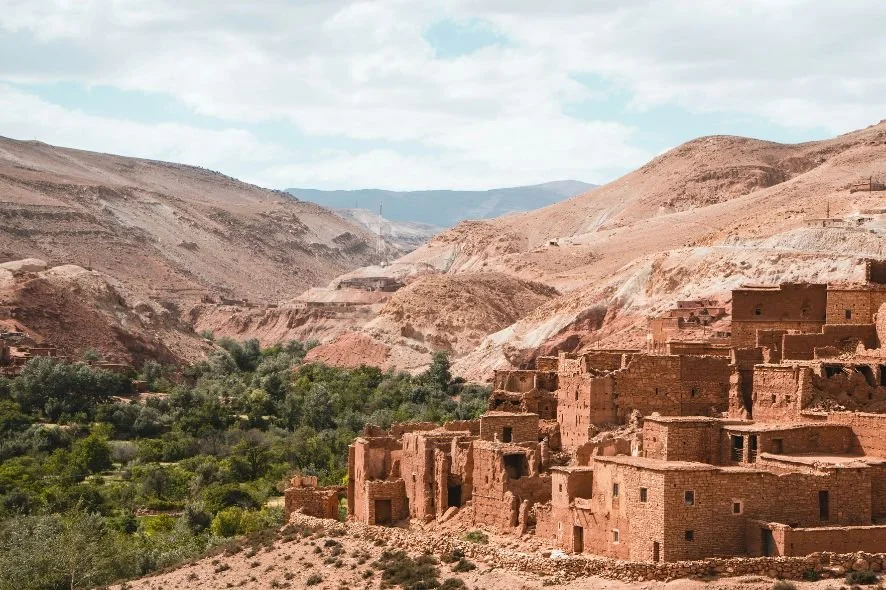 A desert landscape with rugged hills and an ancient village made of adobe buildings on a hillside.