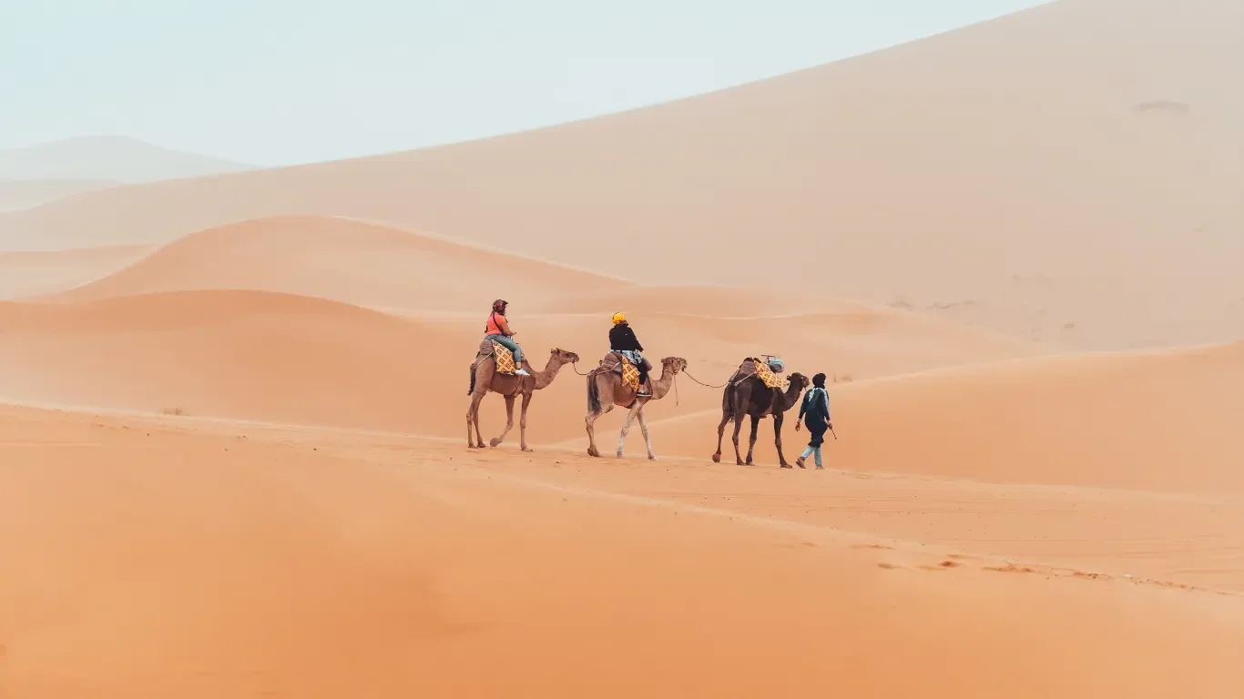 People riding camels through a desert with sand dunes