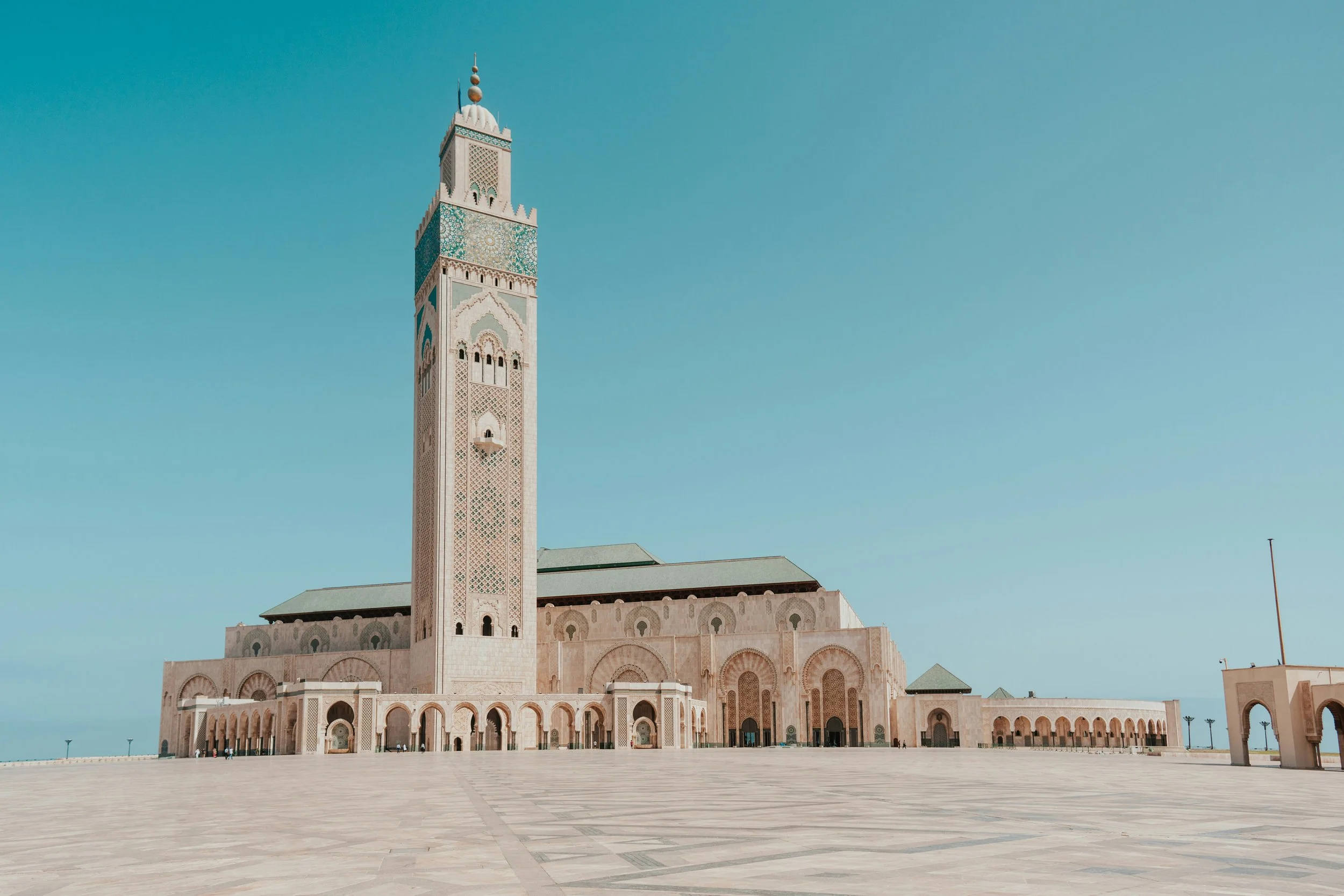 The Hassan II Mosque in Casablanca, Morocco, featuring a tall minaret, intricate tile work, and a spacious courtyard under a clear blue sky.