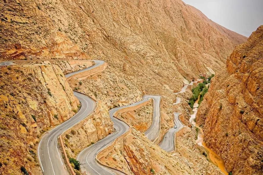 A winding mountain road with sharp switchbacks descends through a rocky canyon with sparse vegetation.
