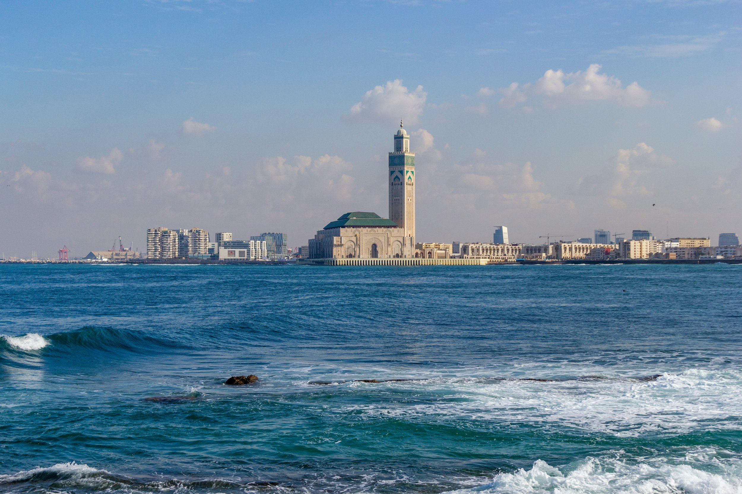 A view of the city of Casablanca, Morocco, with the Hassan II Mosque in the foreground, seen across the Atlantic Ocean on a partly cloudy day.
