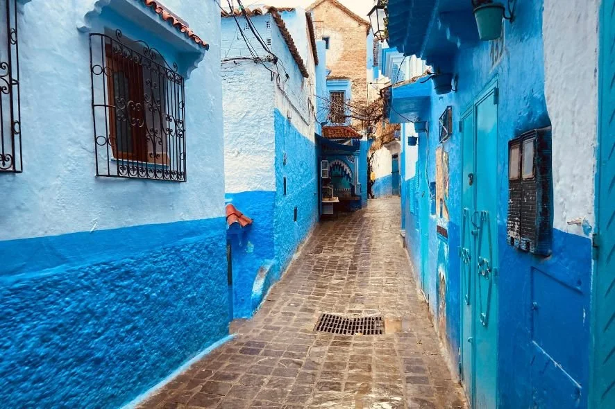 Narrow alleyway with blue-painted buildings on both sides, cobblestone pavement, and decorative iron window grilles.