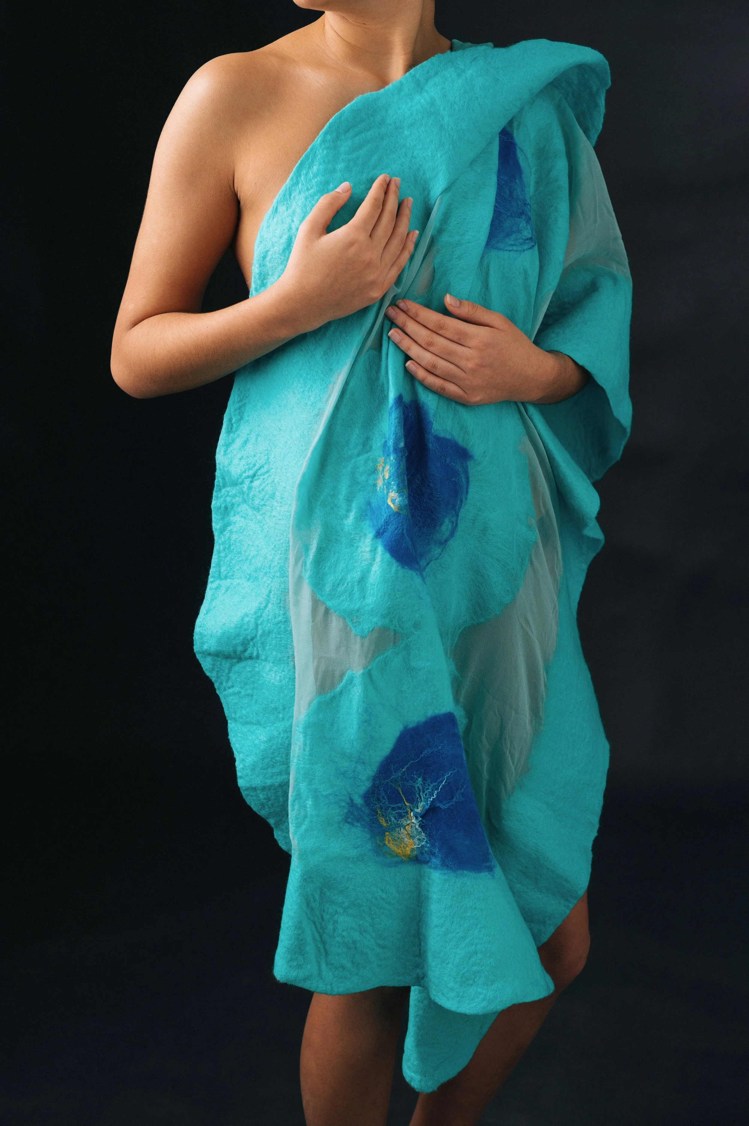 Person holding a blue and teal textured fabric with abstract designs against a dark background.