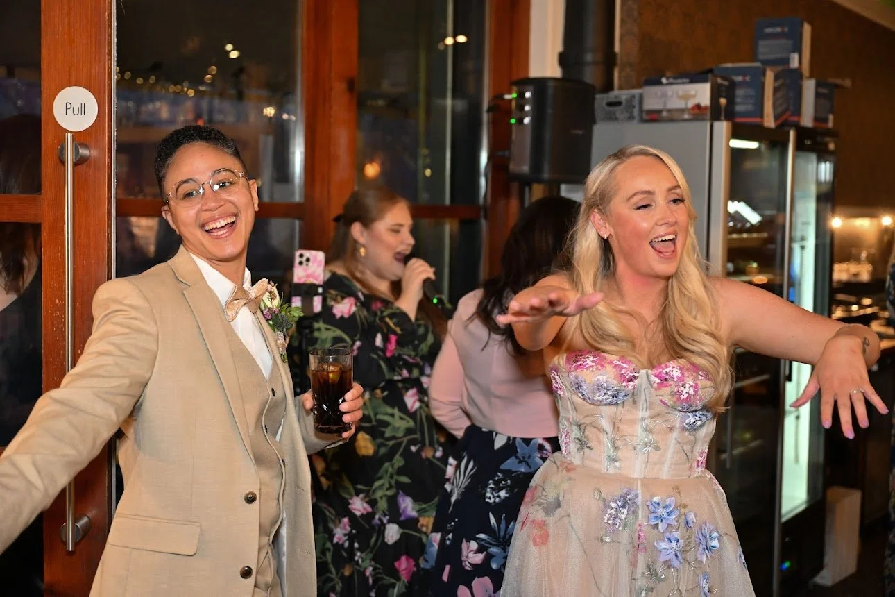 A bride in a white dress with floral embroidery, dancing to Emma Katherine Singer who is singing in the background at a wedding in Bristol during the evening turnover