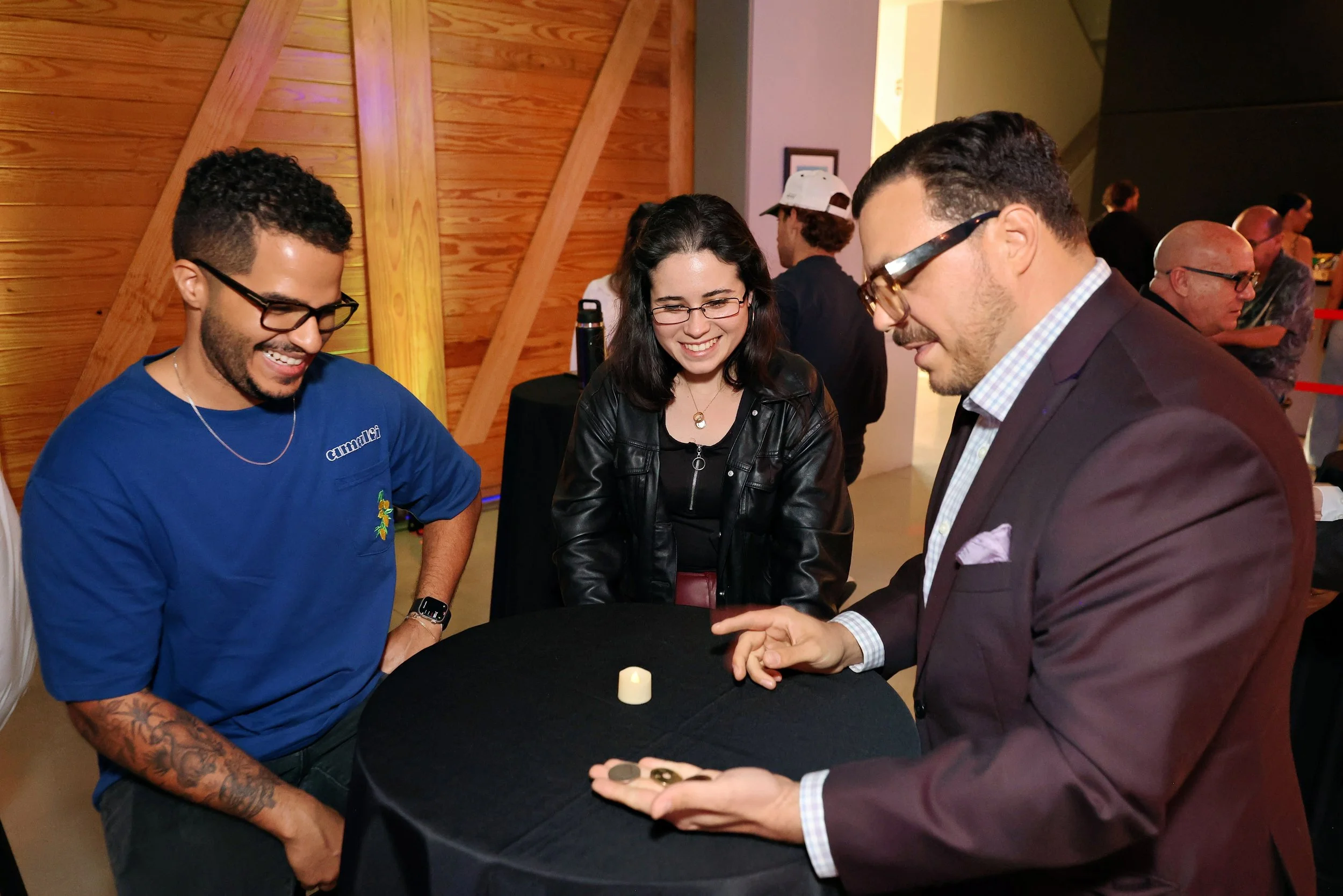Michael Andrew performing close-up magic for guests gathered around a cocktail table at a Miami event.