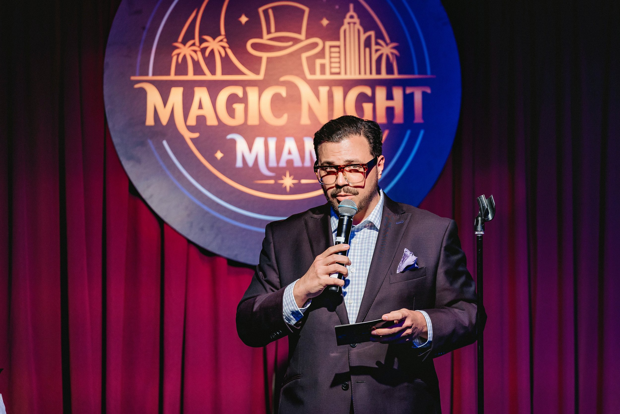 Michael Andrew hosting Magic Night Miami onstage with a microphone.