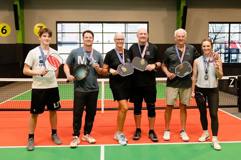 Pickleball players stand in a line with their paddles and medals after a tournament.