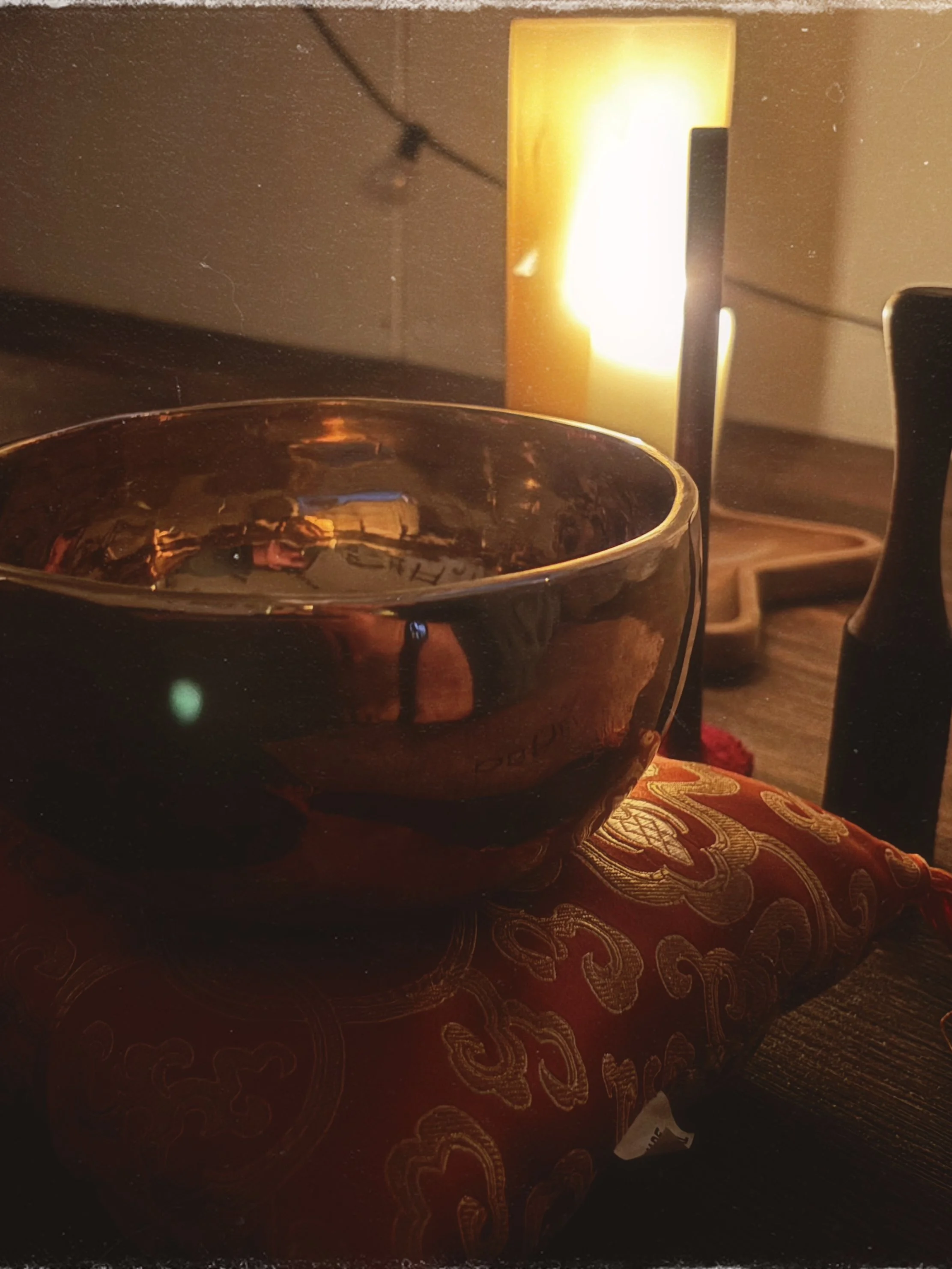 A tibetan singing bowl sits on a yoga mat beside a glowing candle.