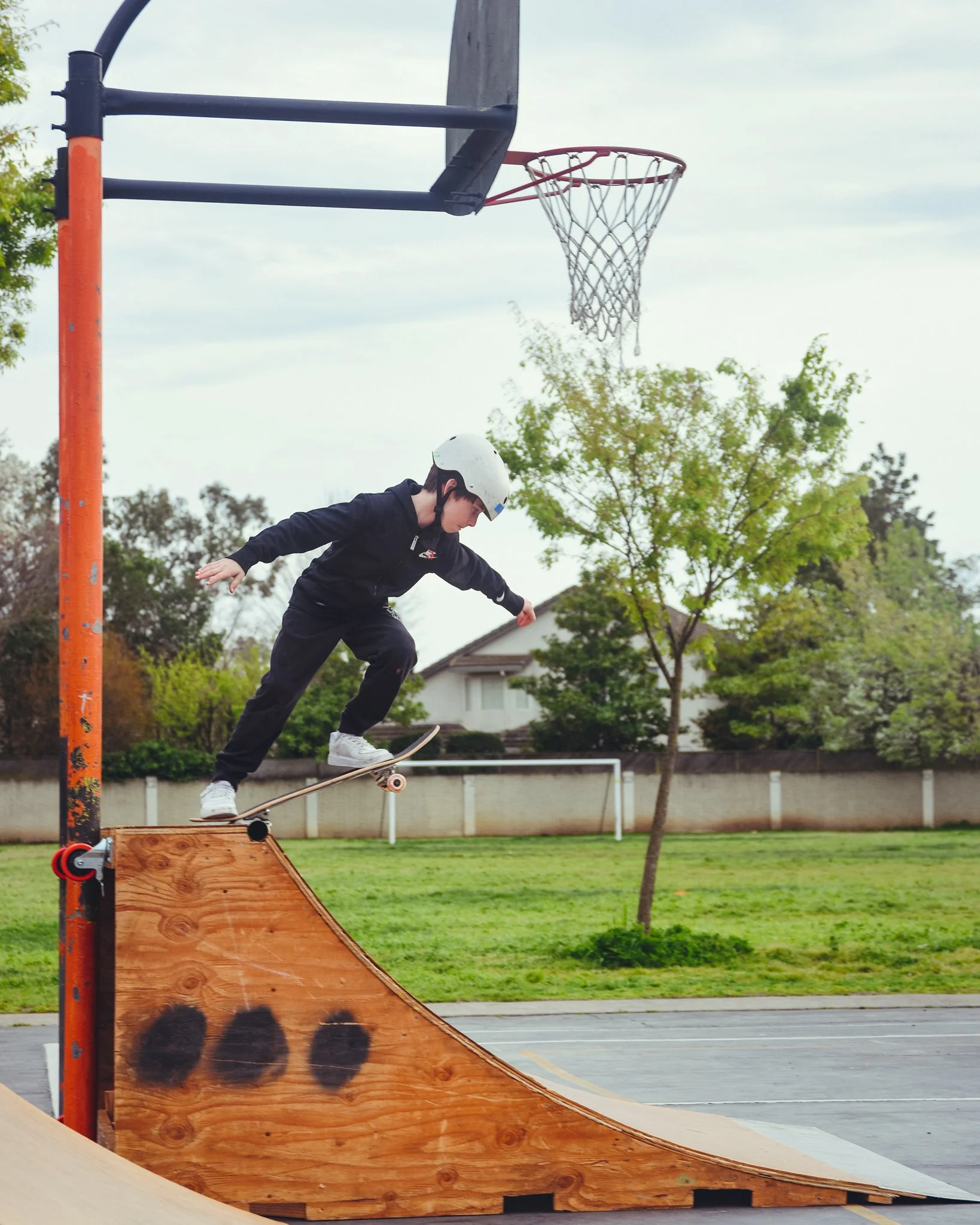 A young skateboarder wearing a helmet balancing on a skateboard on a wooden ramp near a basketball hoop at a skate night.
