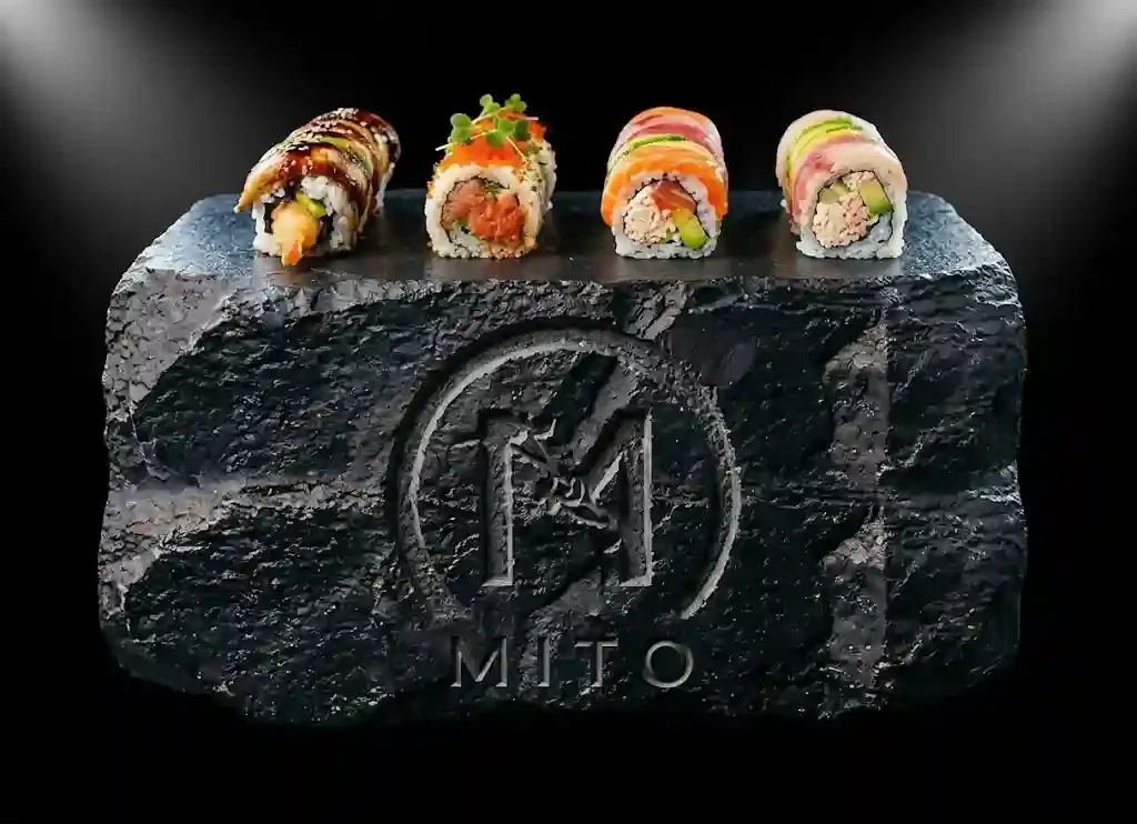 Assorted specialty sushi rolls at Mito Hibachi & Sushi in Warren, Michigan, featuring the Dragon Roll, California Roll, Rainbow Roll, Spicy Tuna Roll, and Philadelphia Roll served on a black stone slab