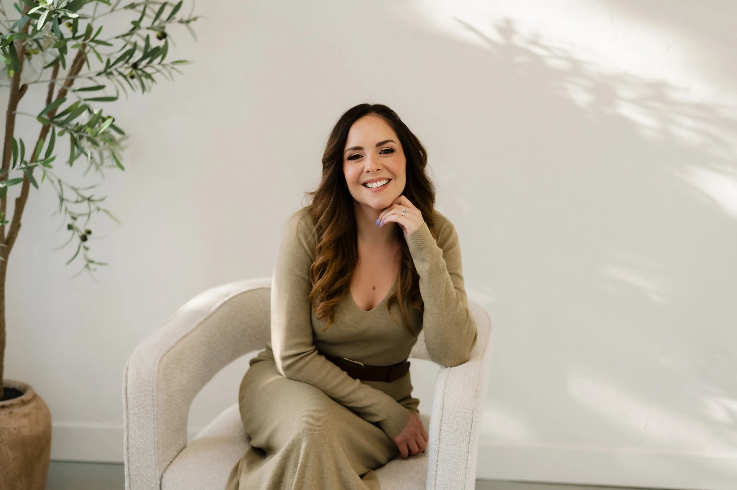 Dr Teela Tomassetti smiling while sitting on a light-coloured therapy chair, waiting to have a consultation or therapy session to help you get on a better path.