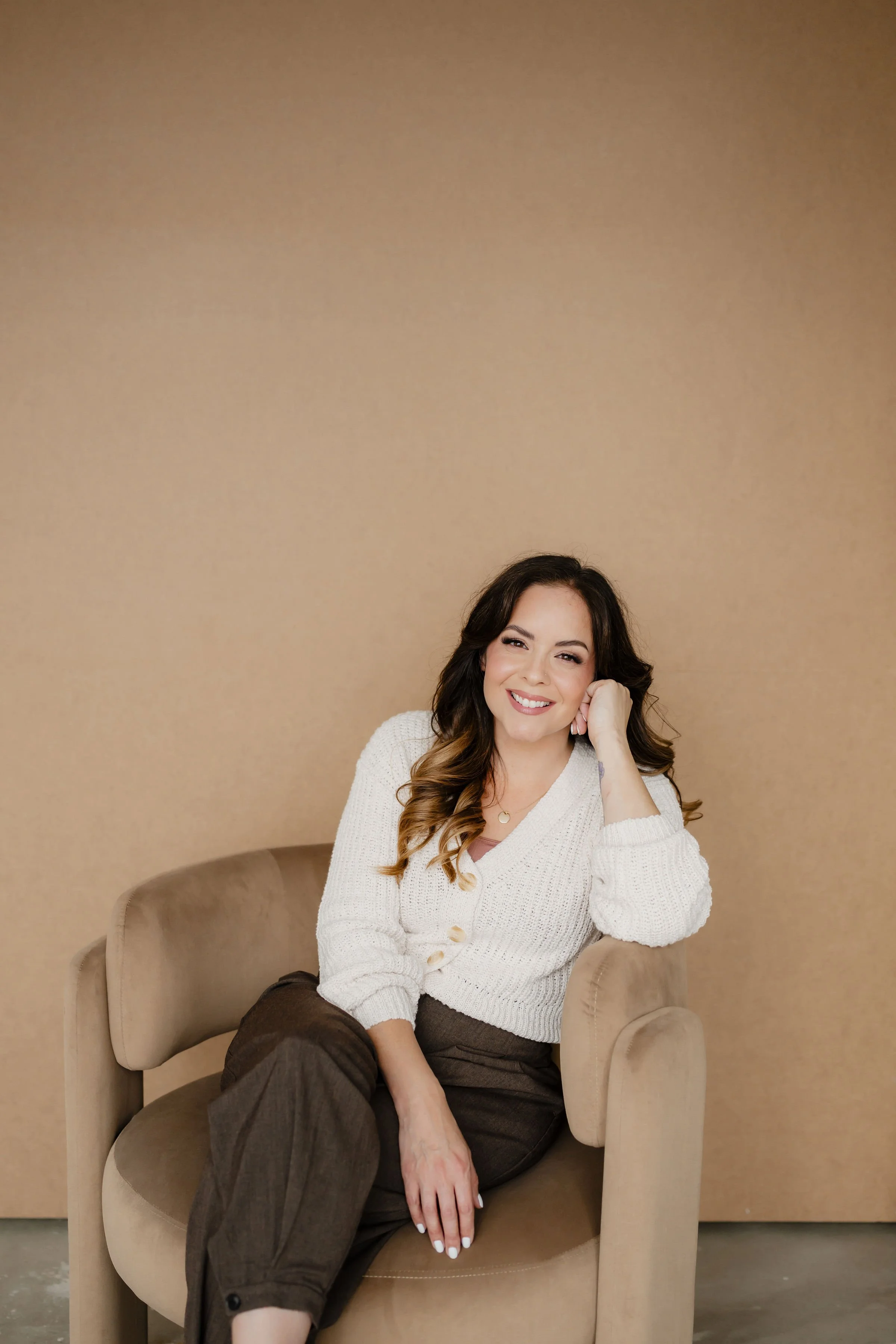 Dr Teela Tomassetti smiling while sitting on a light-coloured therapy chair, waiting to have a consultation or therapy session to help you get on a better path. 
