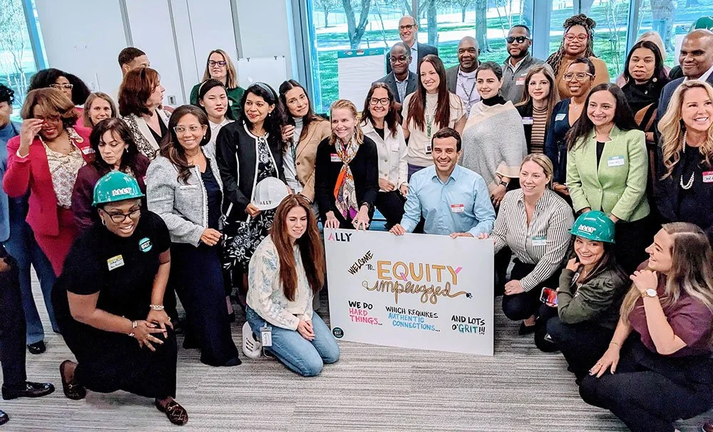 Group of diverse people posing indoors with a banner that reads 'Equity Unplugged' and mentions hard work, authentic connections, and grit. Some hold helmets with 'Ally' branding.