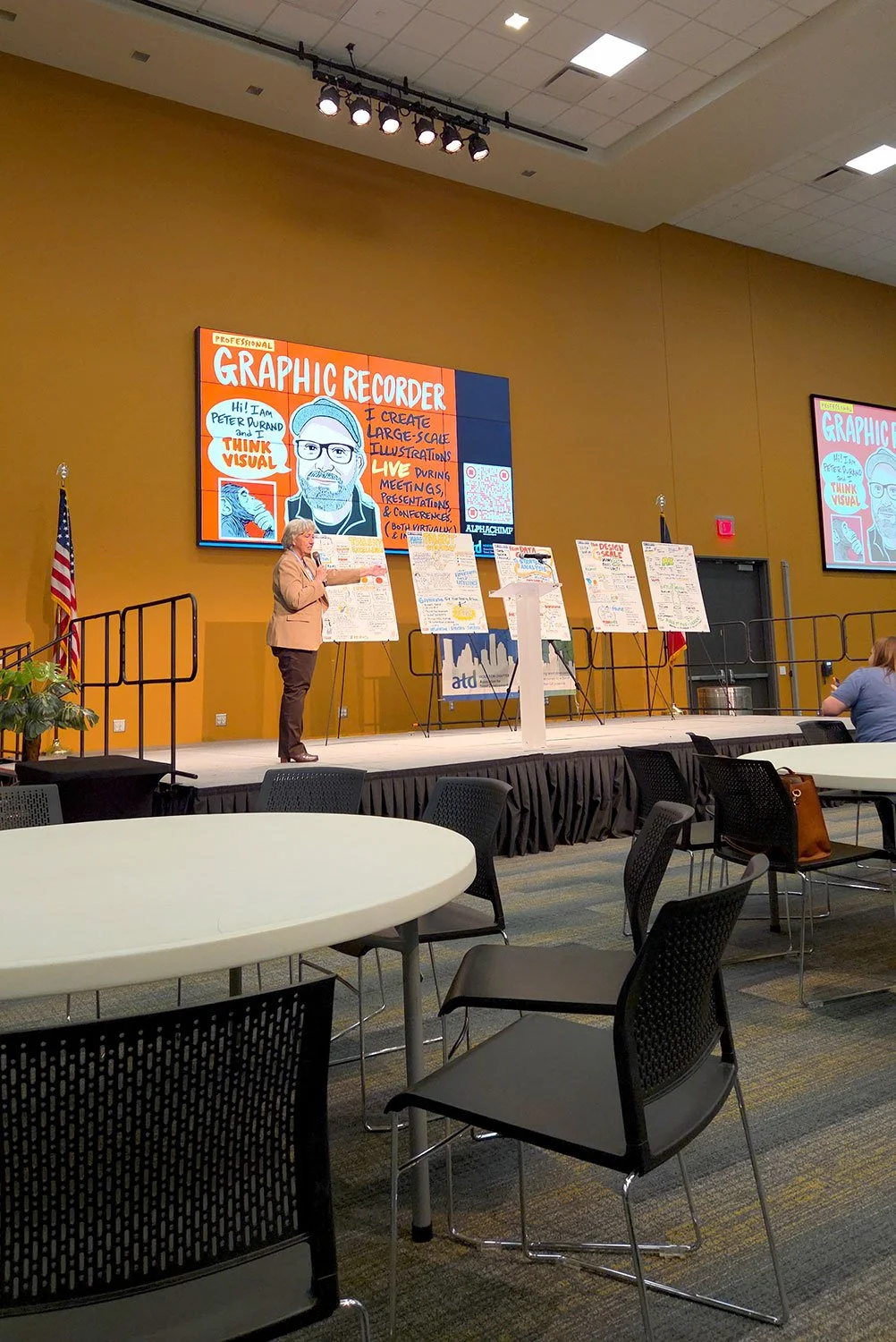 ATD Houston President Carol Jennings on stage with graphic recording and Peter Durand's giant face.